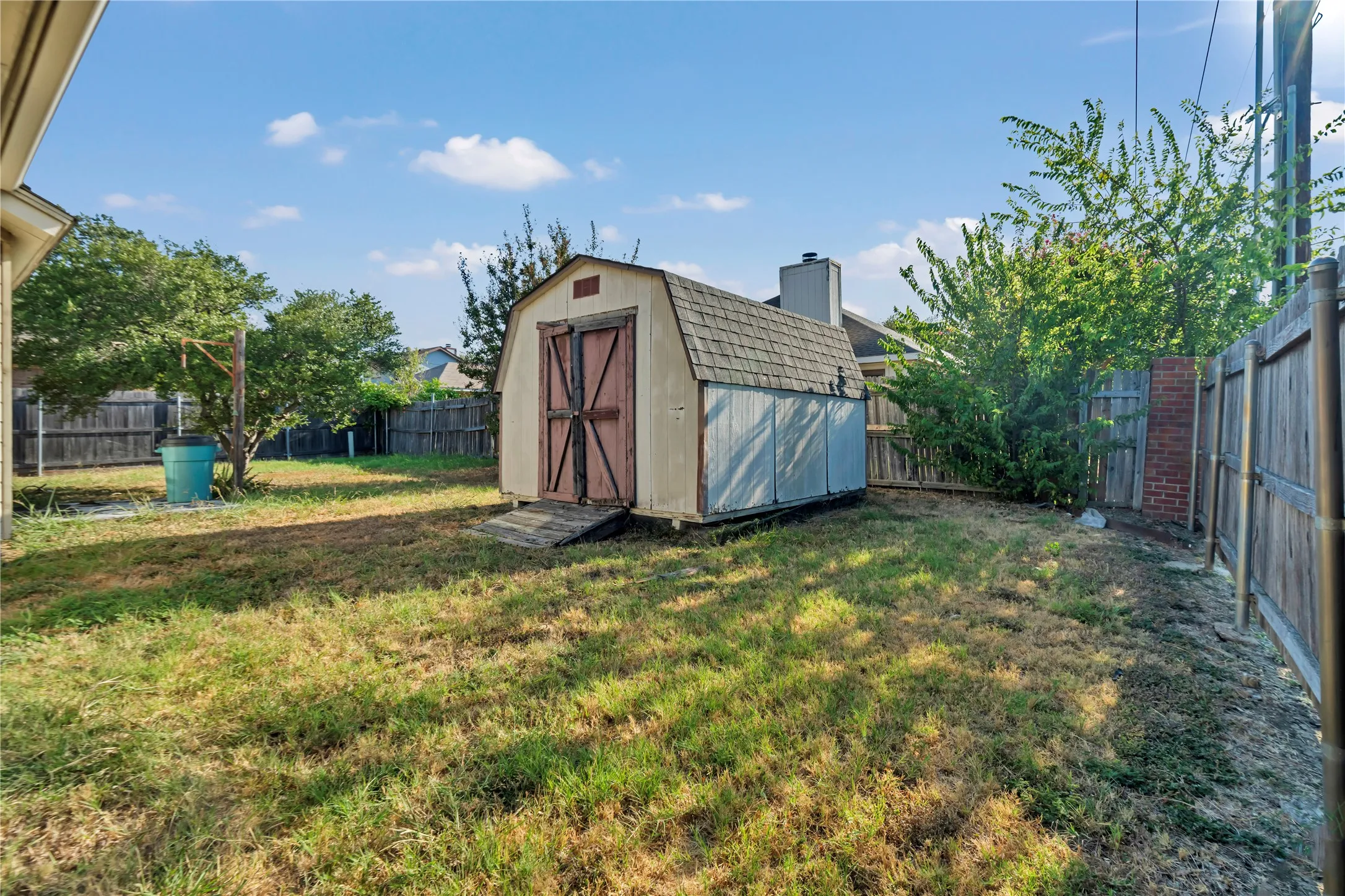 Fenced backyard featuring a storage shed with a gambrel roof and double barn doors