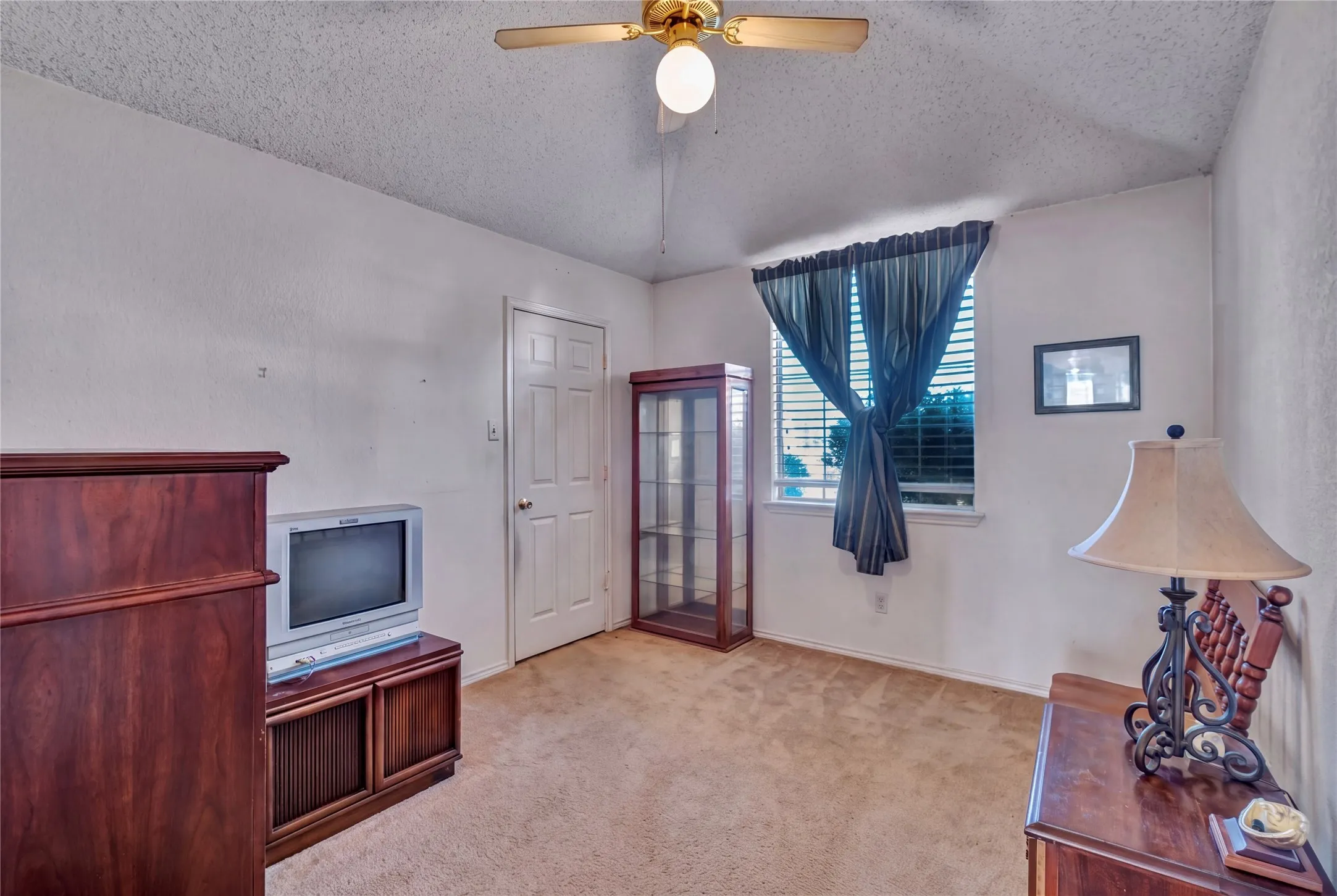 Carpeted flooring, window with blinds, ceiling fan with light fixture, and a paneled interior door