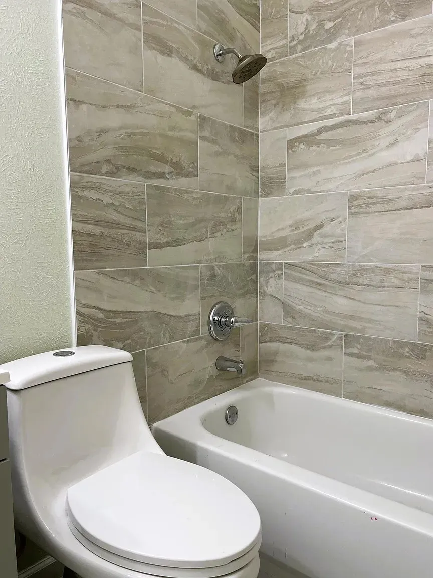 Bathtub with integrated shower head, chrome fixtures, and tiled surround