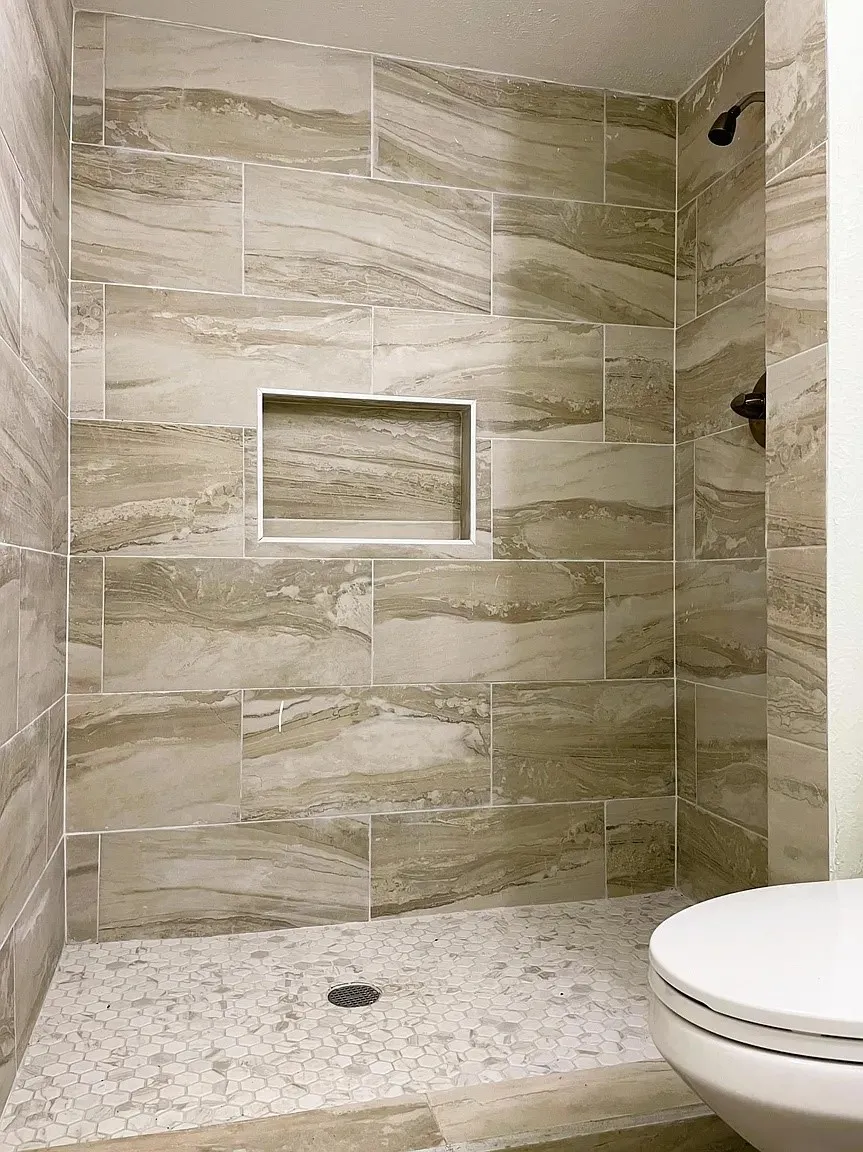 Tiled shower enclosure featuring rectangular wall tiles with naturalistic veining, a recessed shower niche, and a contrasting hexagonal mosaic floor