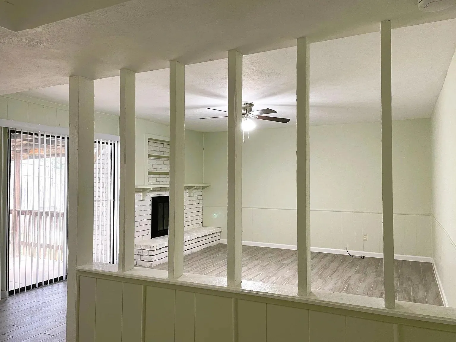 Living area with wood-finish flooring, a white brick fireplace, and a ceiling fan