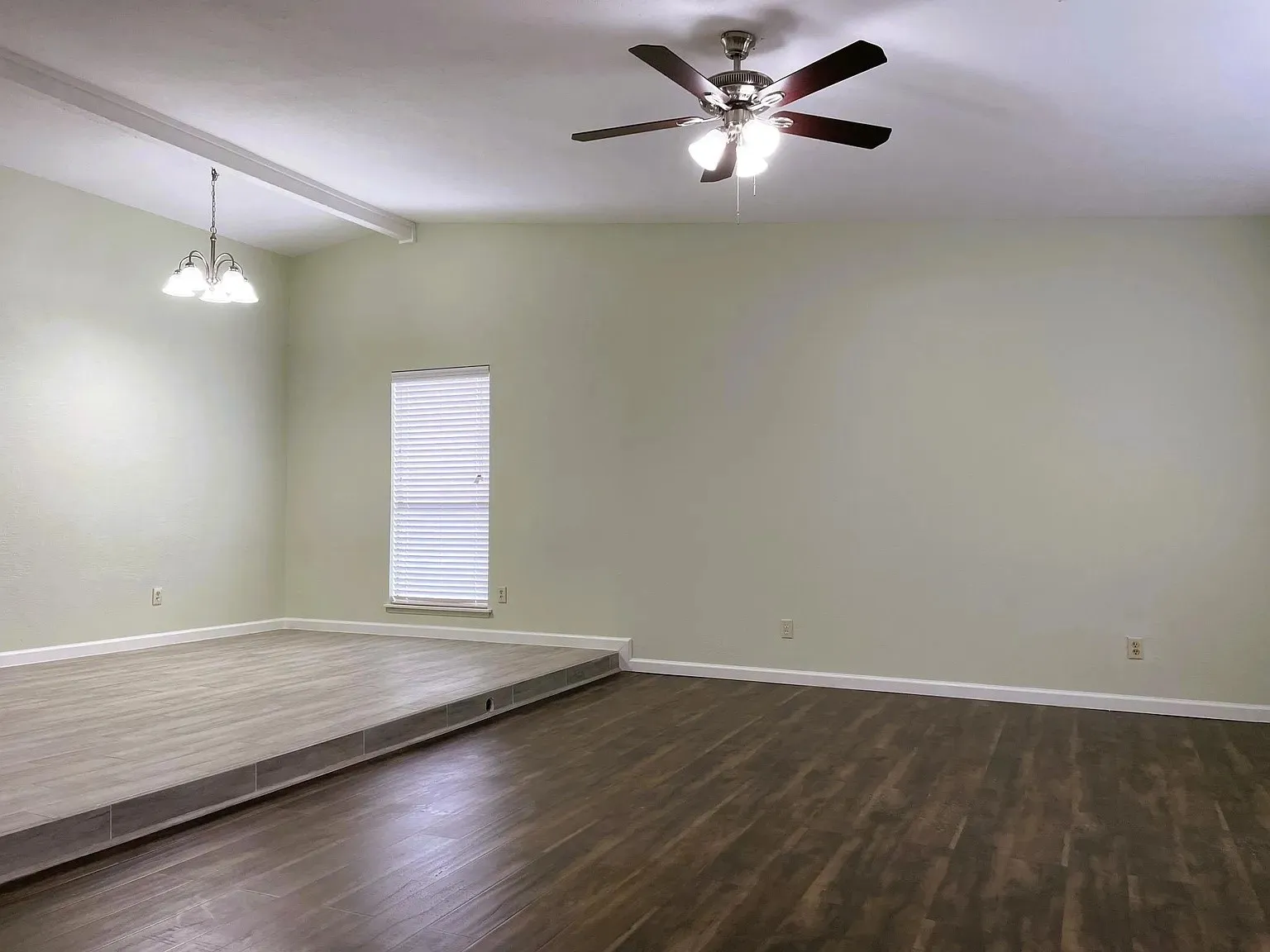 Spacious room featuring wood-finish flooring, a raised platform with wood-finish flooring, a ceiling fan with integrated lighting, and a pendant light fixture