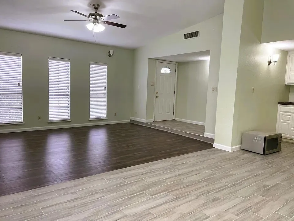 Vaulted ceiling with a ceiling fan, three windows with blinds, wood-finish flooring, and light-toned tile flooring