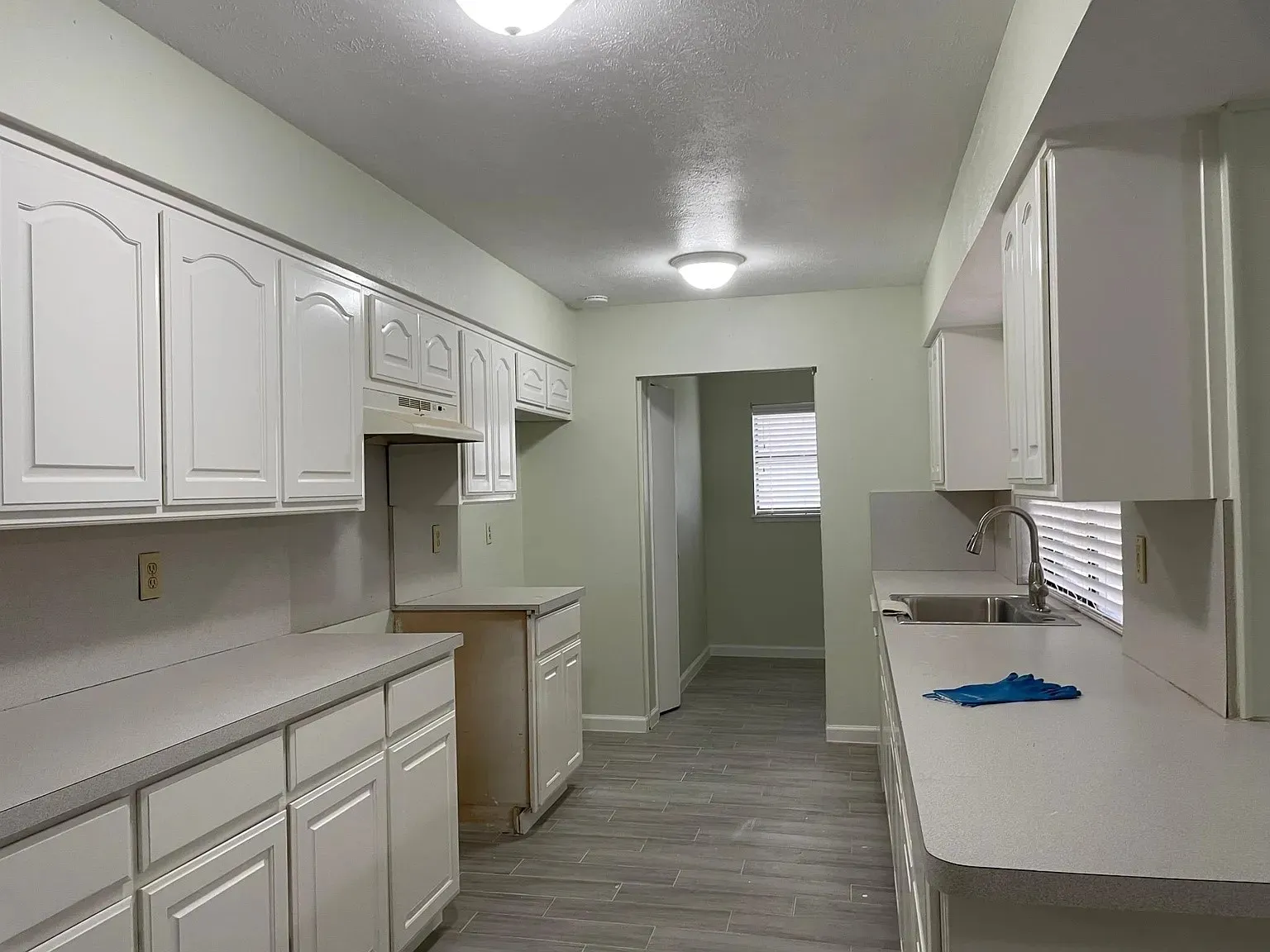 White cabinetry with arched panel doors, light-toned countertops, stainless steel sink with a gooseneck faucet, and wood-look tile flooring