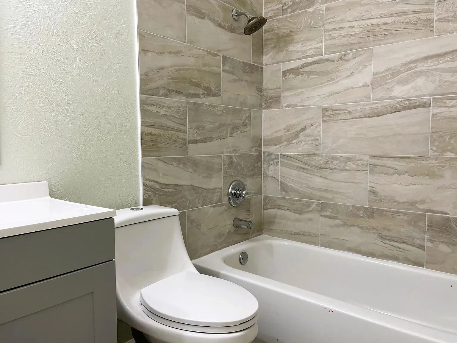 Bathtub featuring a shower with large format tile surround