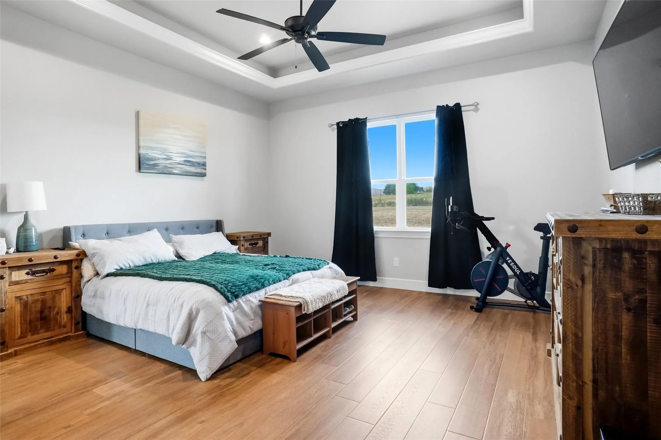 Tray ceiling with a ceiling fan, wood-finish flooring, and large window