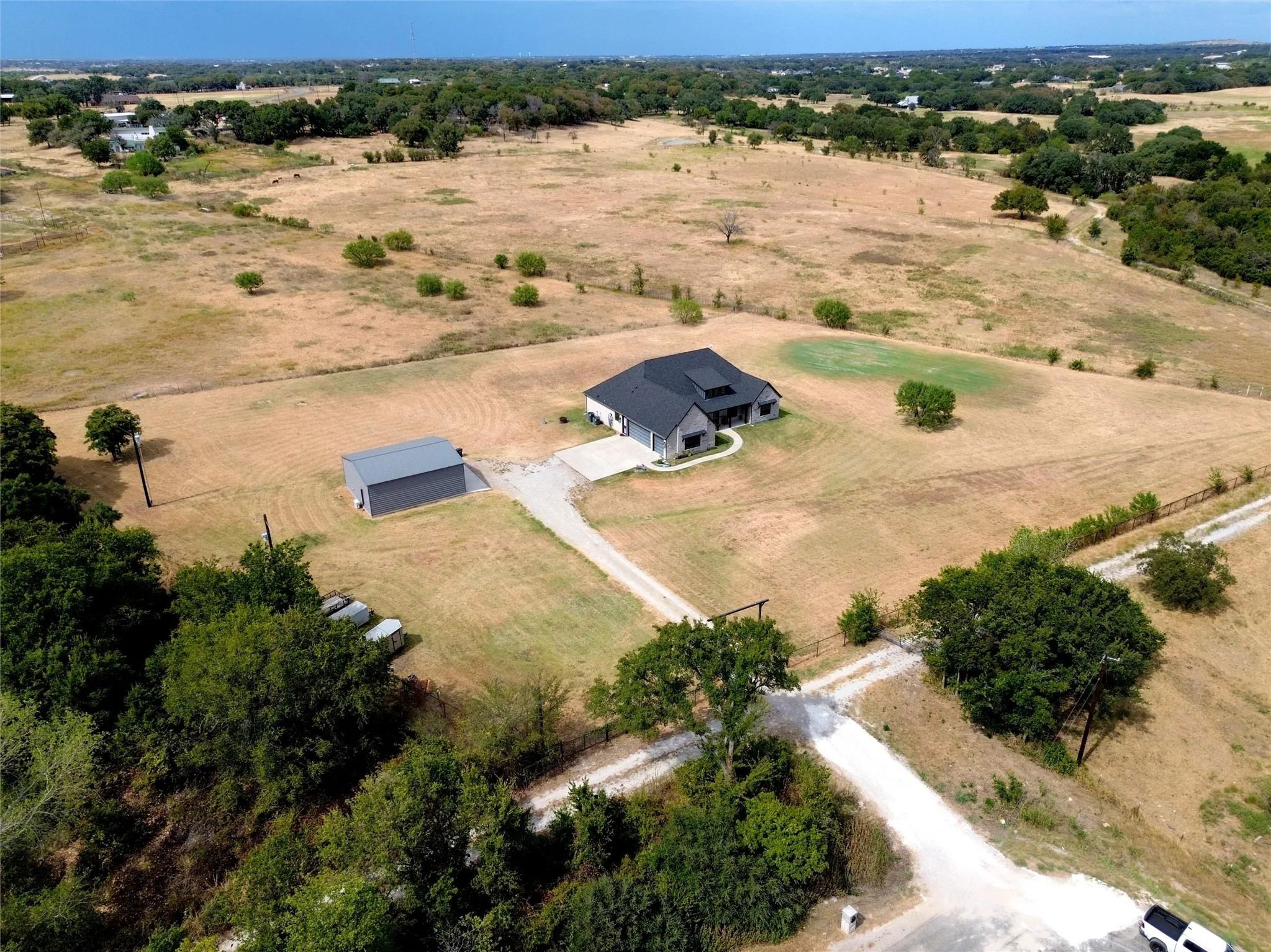 Expansive rural setting with a modern home, gravel driveway, and a detached metal building