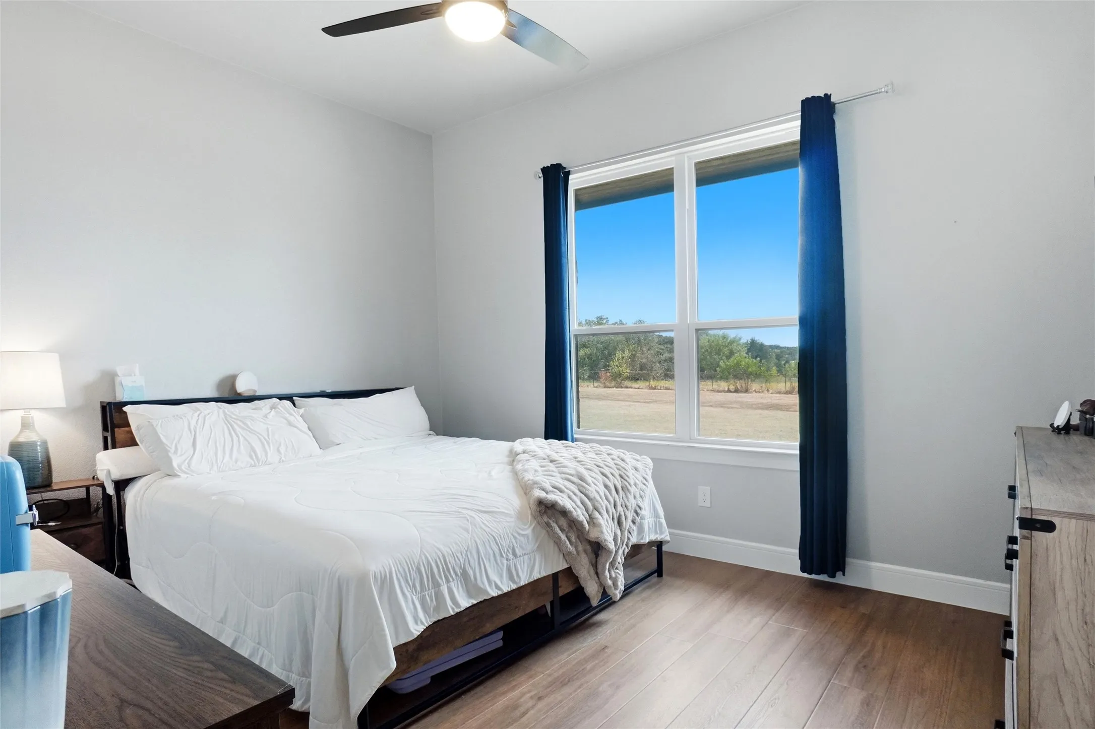 Wood-finish flooring, ceiling fan with integrated lighting, and a large window with outdoor scenery