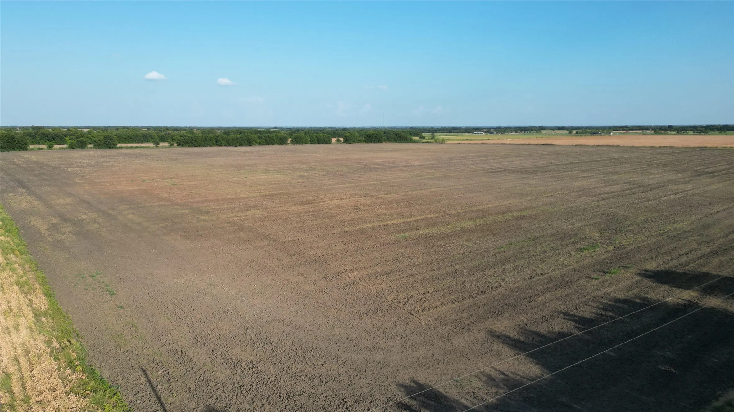 Expansive cultivated land with distant tree lines under a clear sky