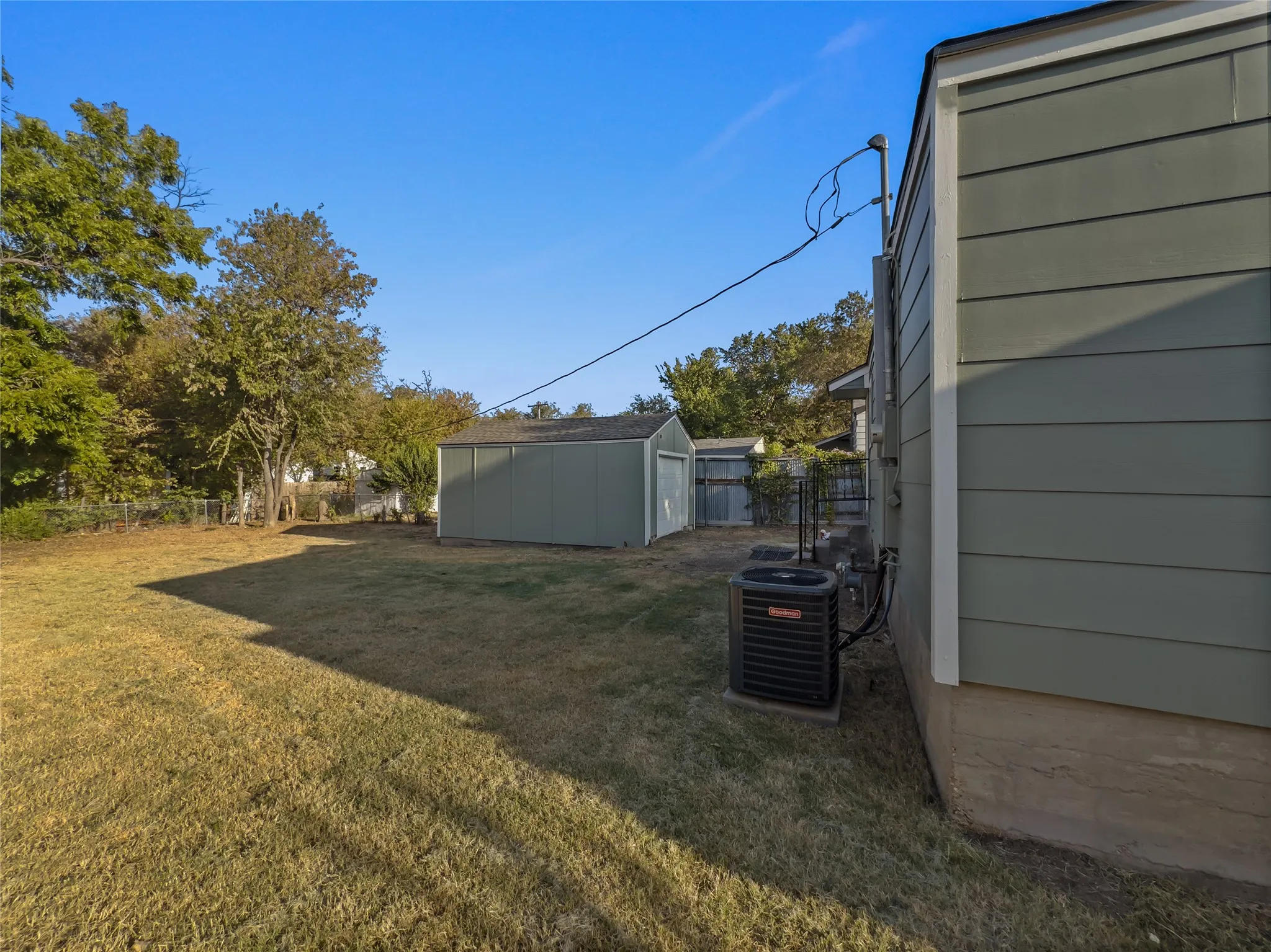 Expansive backyard with a separate storage shed, mature trees, and a visible HVAC unit