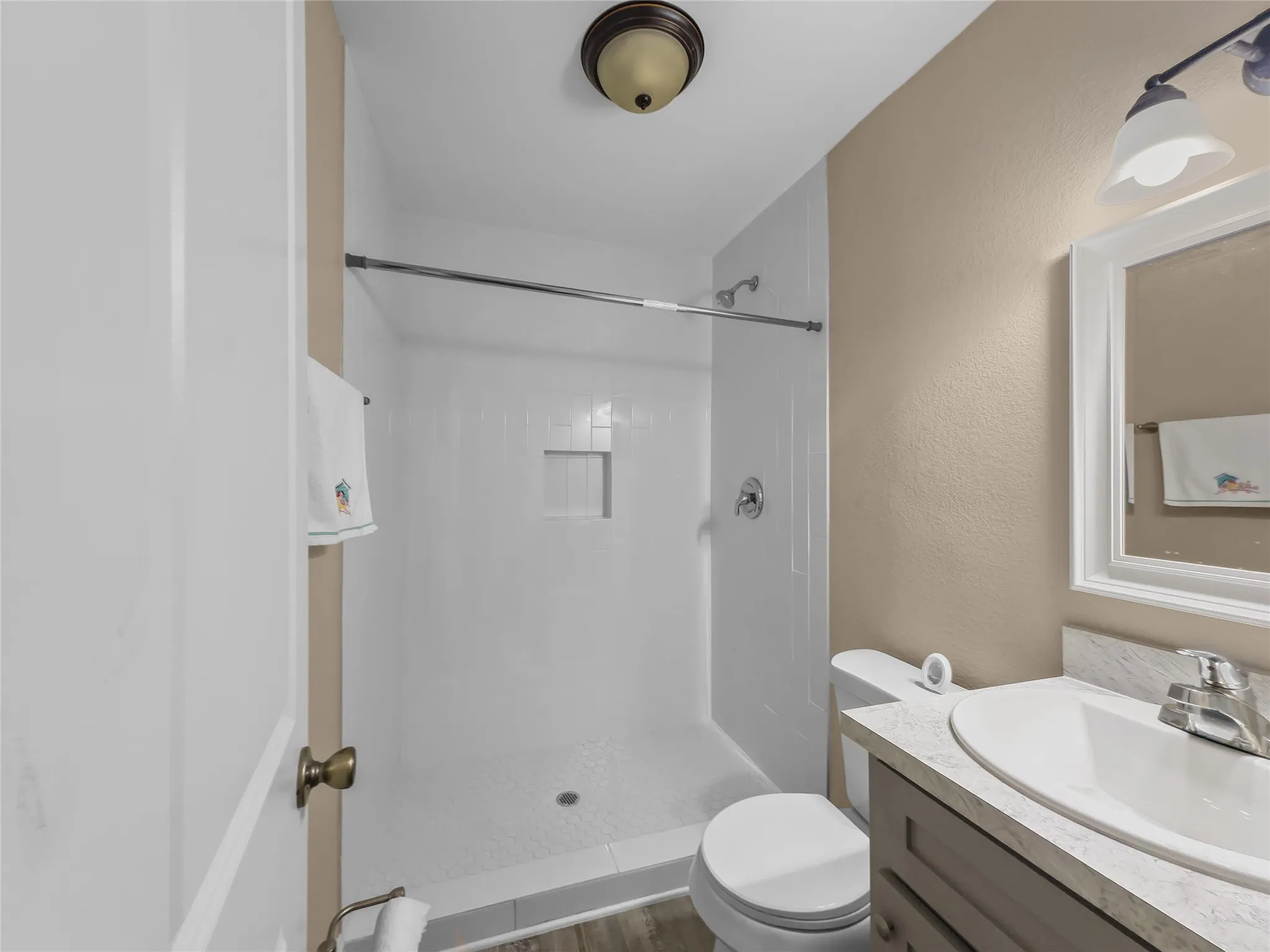 White-tiled shower with built-in niche, chrome fixtures, and a white vanity with an integrated sink