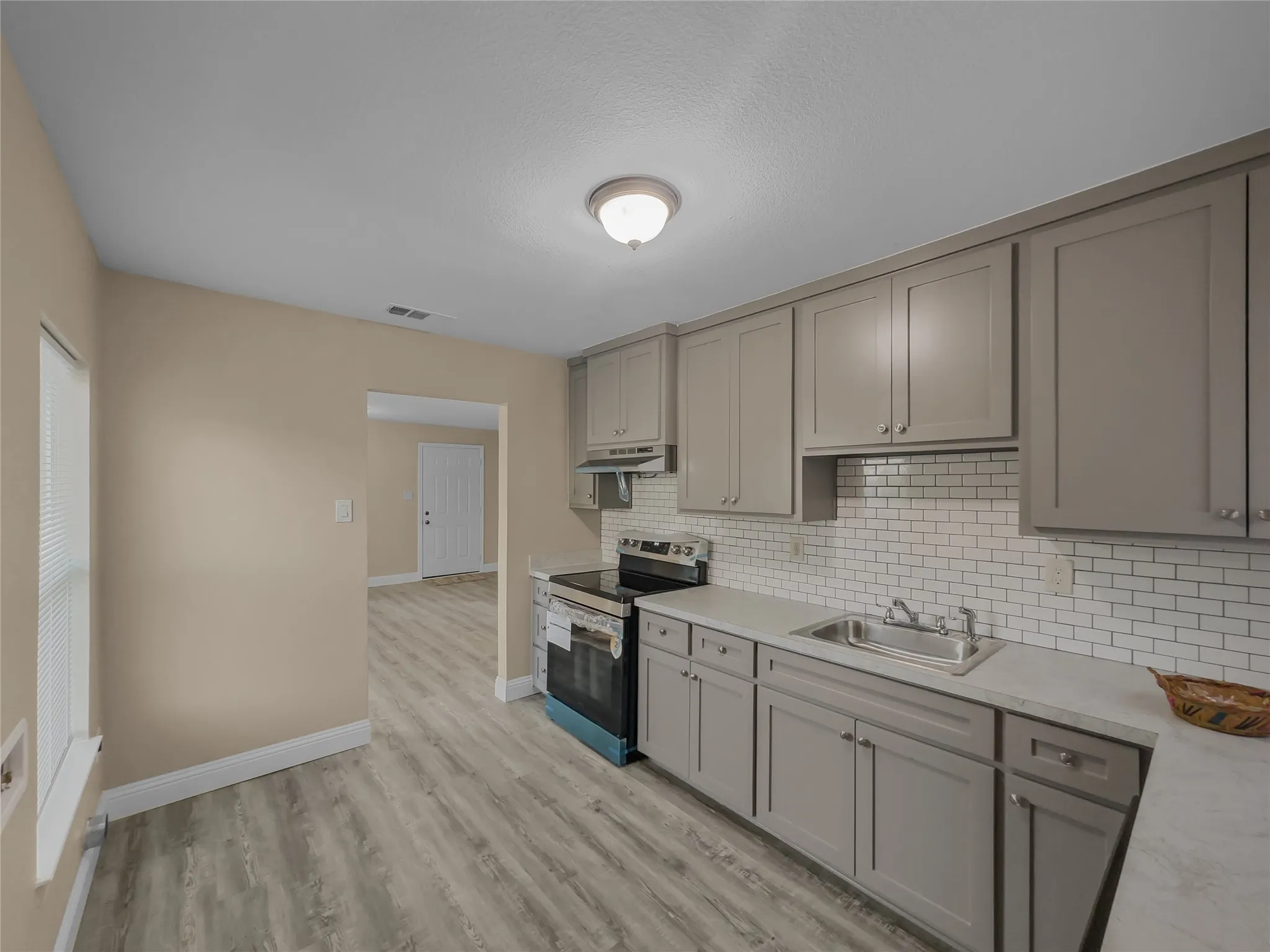 Kitchen featuring grey shaker-style cabinetry, white subway tile backsplash, stainless steel sink, and wood-finish flooring