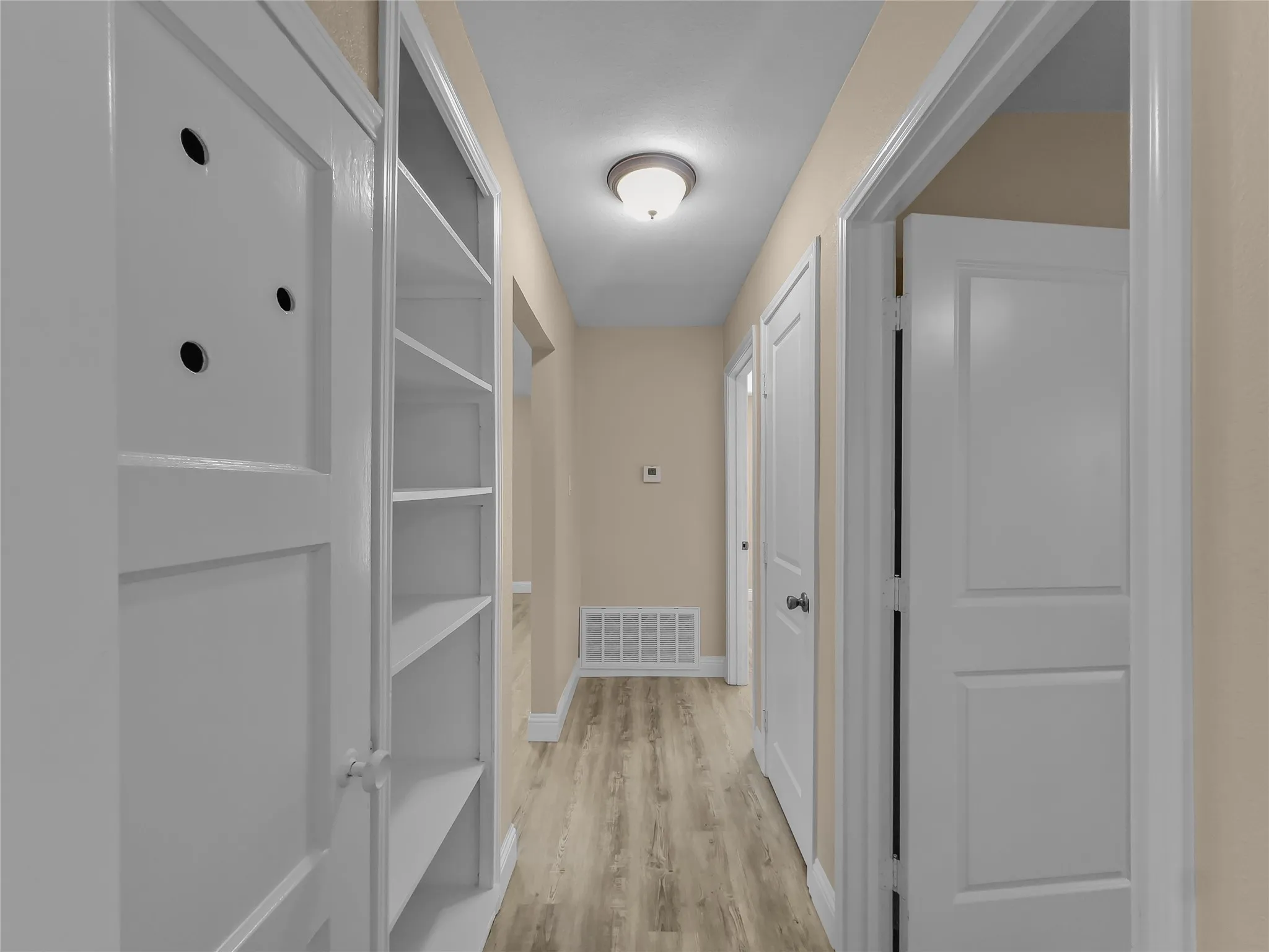 Hallway featuring built-in shelving, panel doors, wood-finish flooring, and recessed lighting