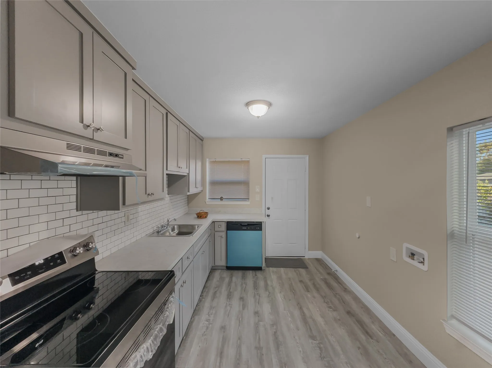 Galley kitchen featuring light gray cabinetry, white subway tile backsplash, stainless steel range, and wood-finish flooring