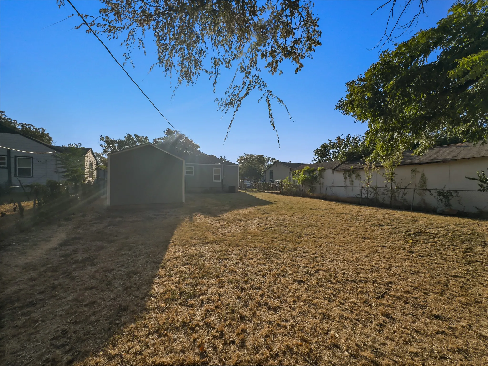 Spacious yard featuring a chain-link fence, mature trees, and a detached storage shed