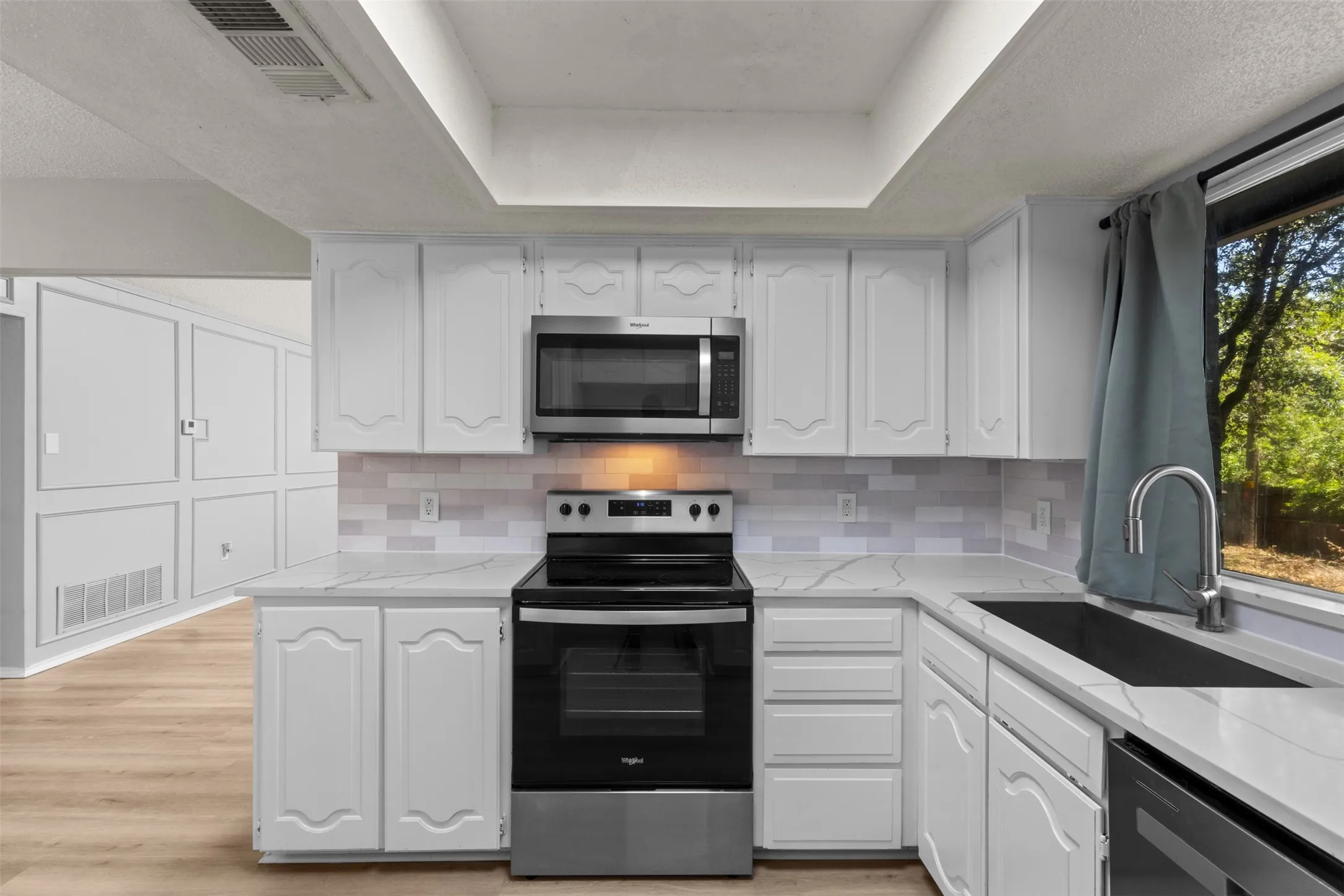 Modern kitchen featuring white cabinetry with raised-panel detailing, stainless steel appliances including a slide-in range and over-the-range microwave, black quartz countertops, subway tile backsplash, and a large island with seating