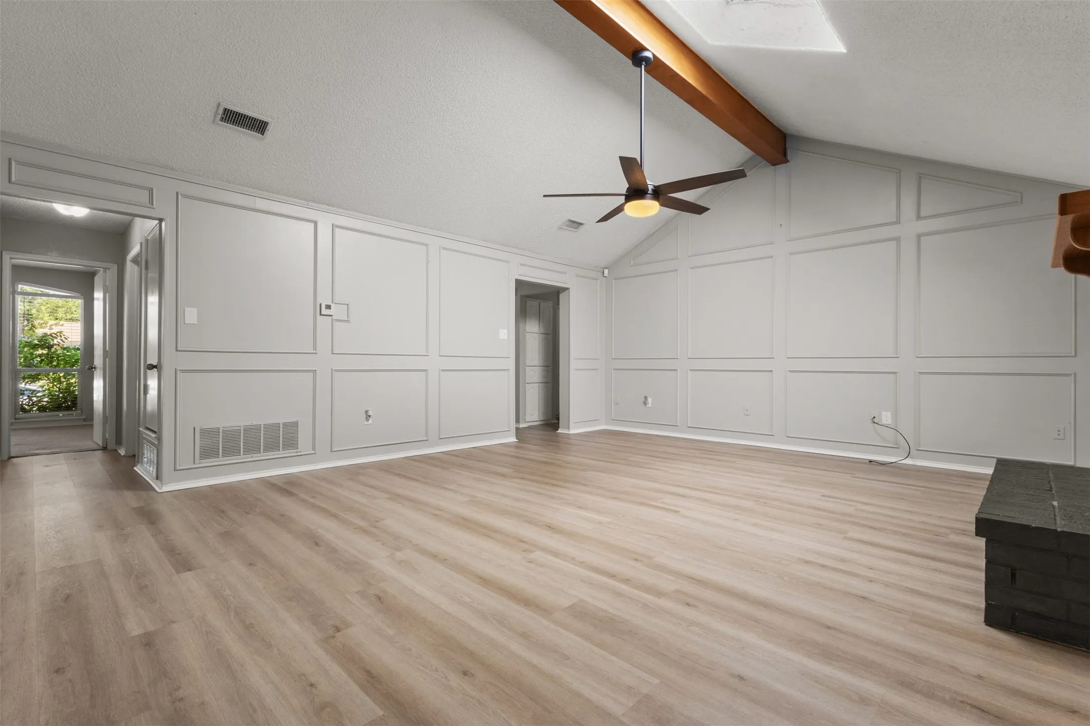 Vaulted ceiling with exposed wood beam, wood-finish flooring, accent wall paneling, and an integrated ceiling fan