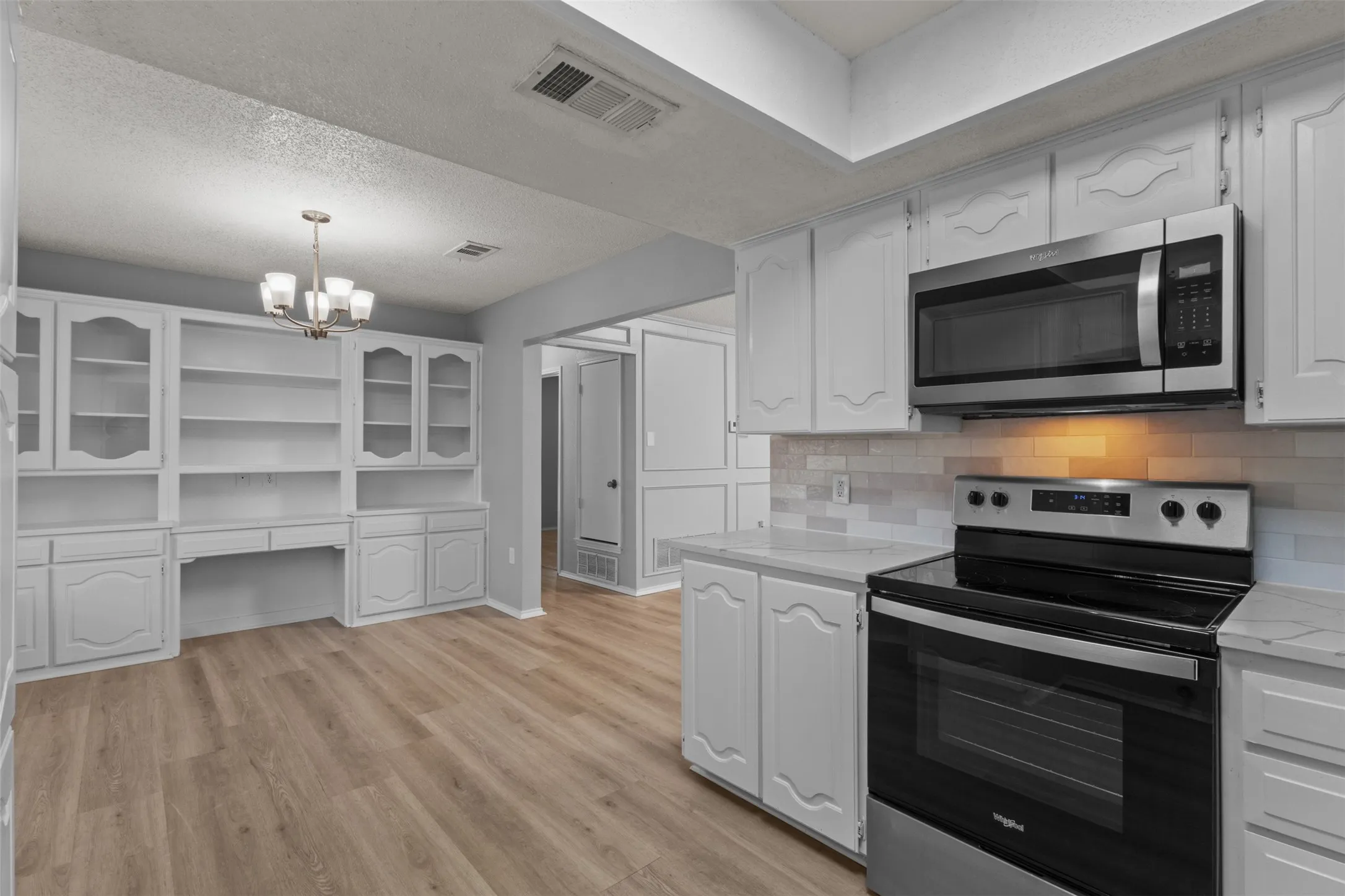 Kitchen featuring wood-finish flooring, white cabinetry, stainless steel appliances, and a tiled backsplash