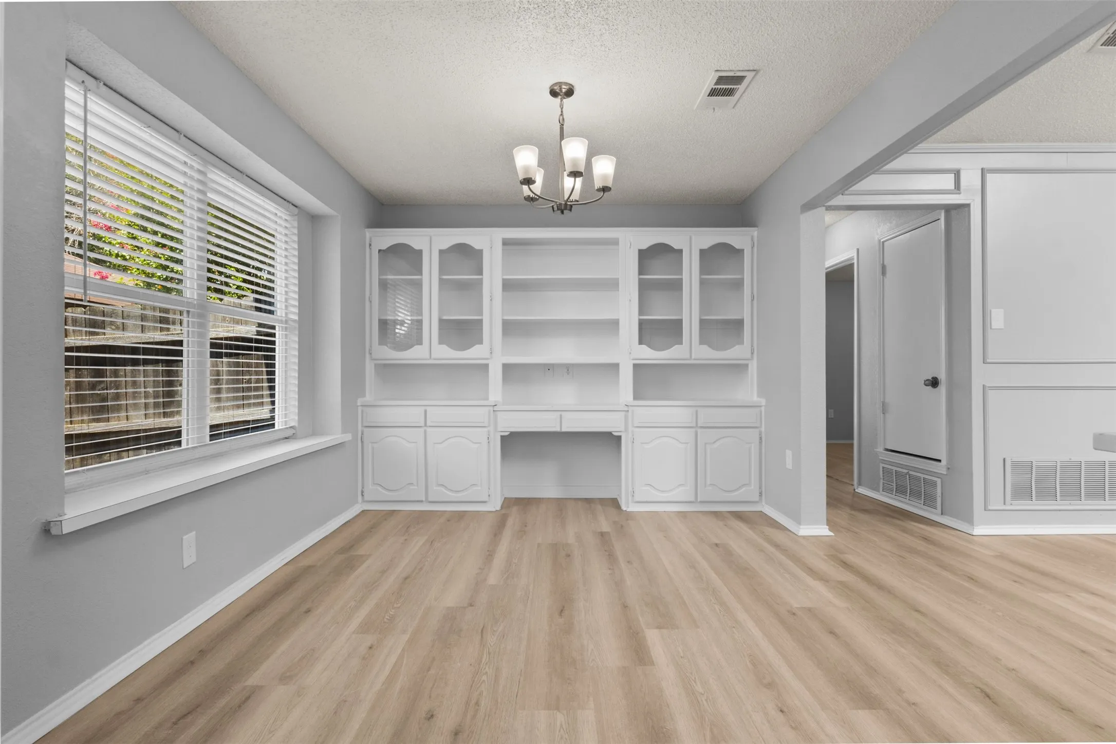 Built-in cabinetry with glass-front uppers, wood-finish flooring, and a multi-light chandelier