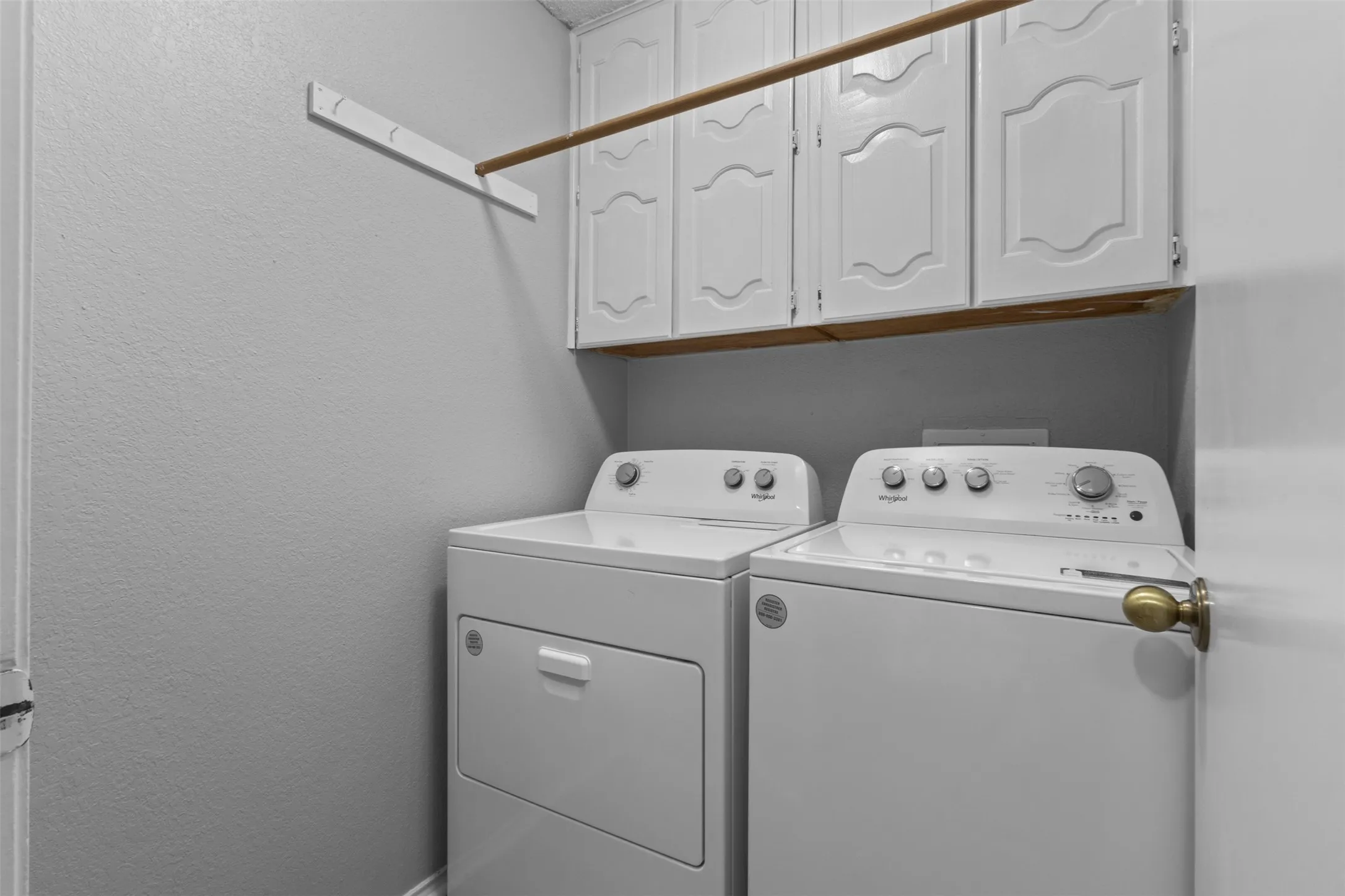 Integrated laundry area featuring white upper cabinetry, a wood-finish hanging rod, and a wall-mounted drying rack