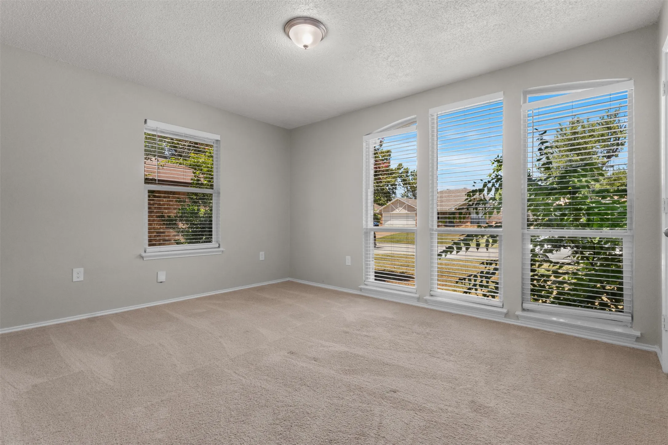 Recessed ceiling light, neutral wall color, three large windows, a single window, and neutral carpeting
