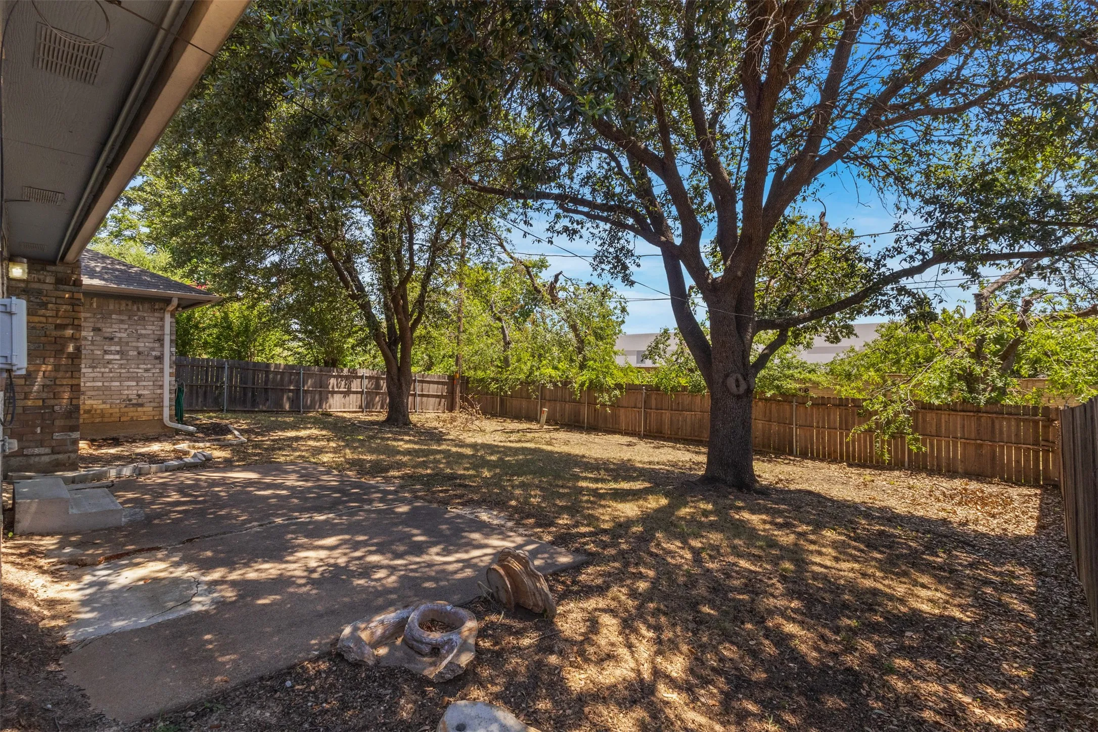 Expansive backyard featuring mature trees, a wood privacy fence, and a concrete patio