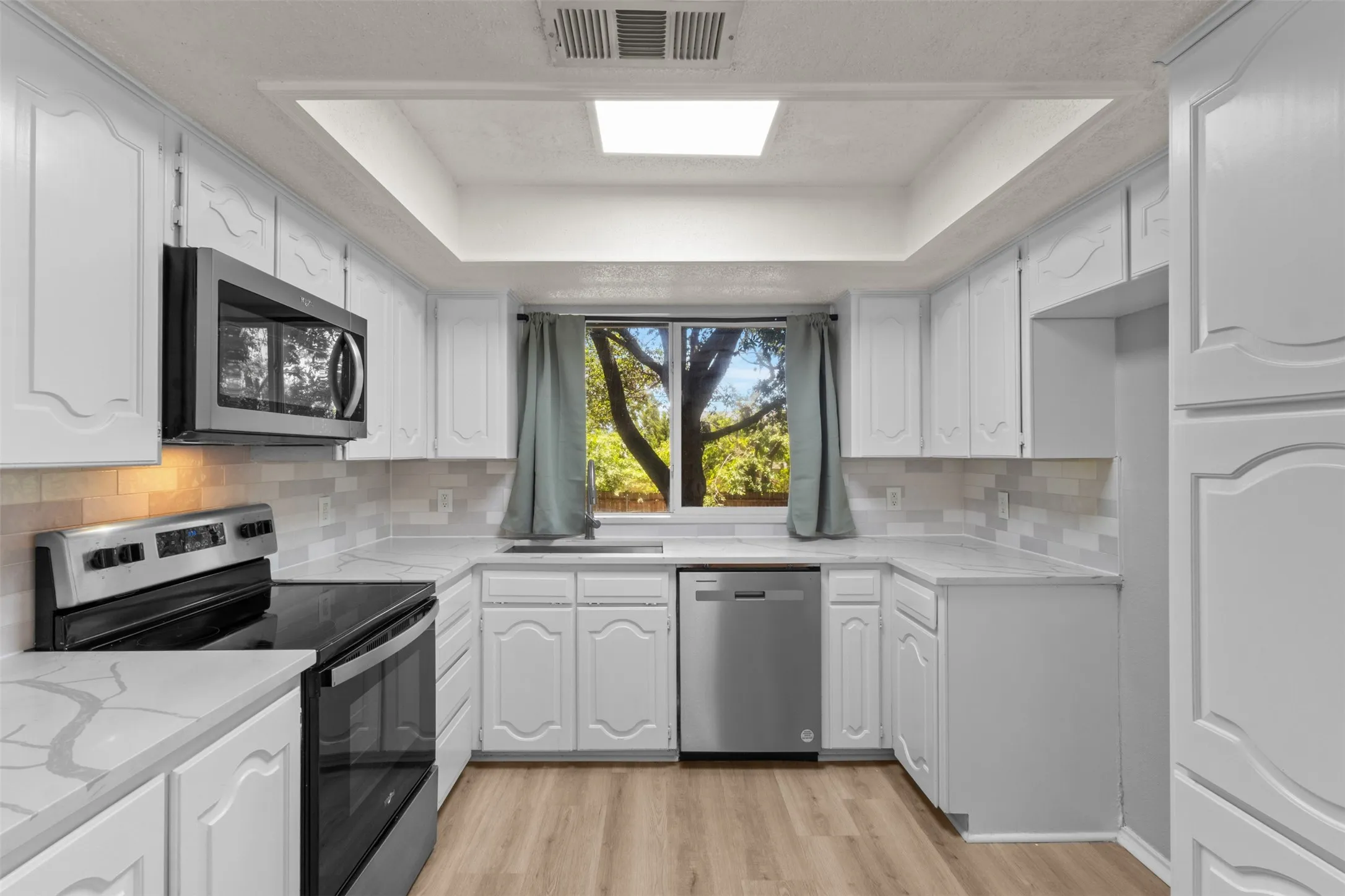 Kitchen featuring white cabinetry, light-toned countertops, a tile backsplash, stainless steel appliances, and wood-finish flooring