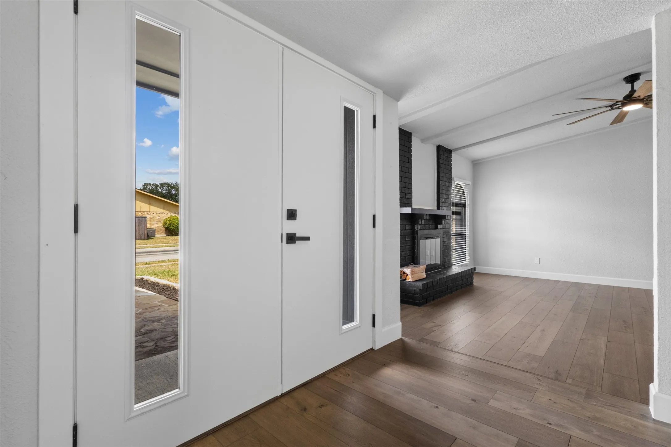 Entryway featuring a solid door with a vertical window, wood-finish flooring, a black brick fireplace, and exposed ceiling beams