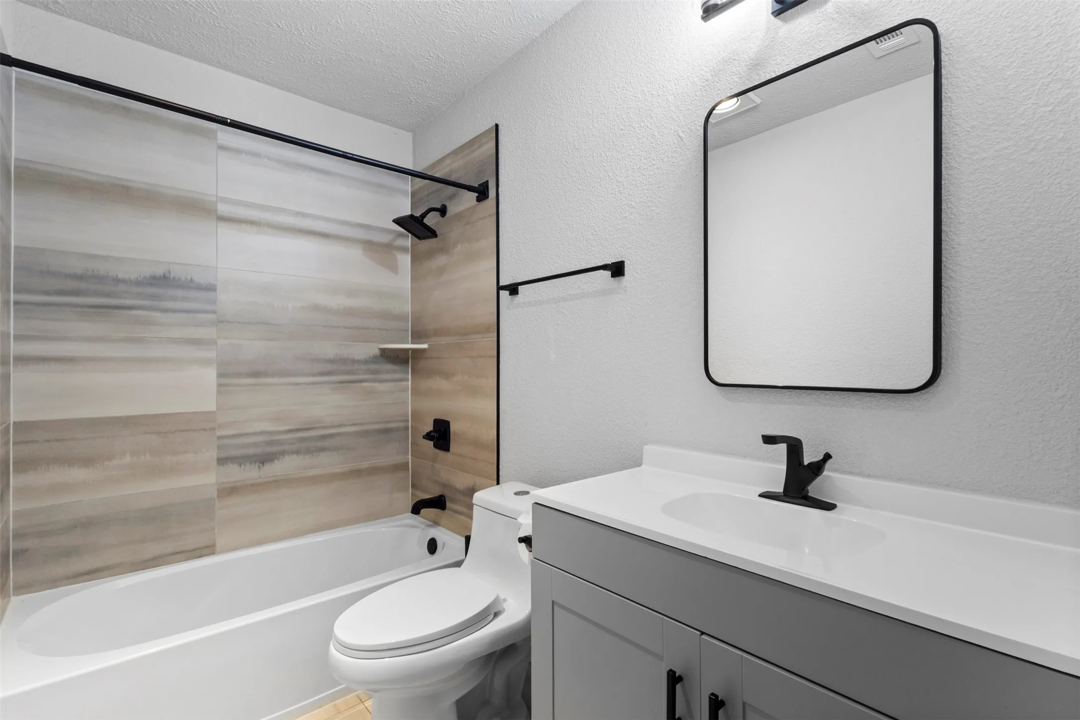 Bathroom featuring a white bathtub, tiled shower surround, gray vanity with white countertop, and a rectangular mirror with a black frame