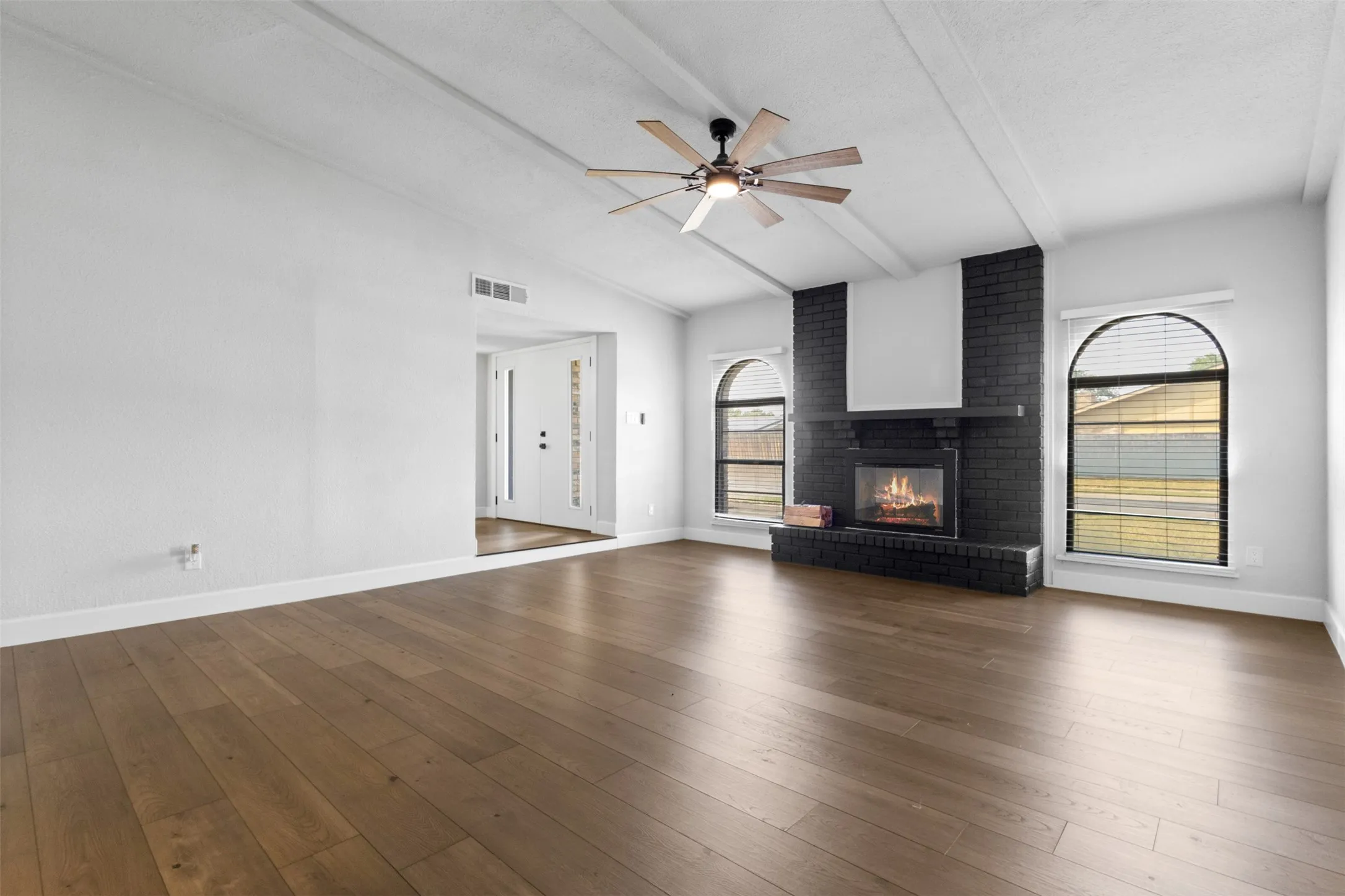 Spacious room with wood-finish flooring, vaulted ceiling with exposed beams, and a ceiling fan