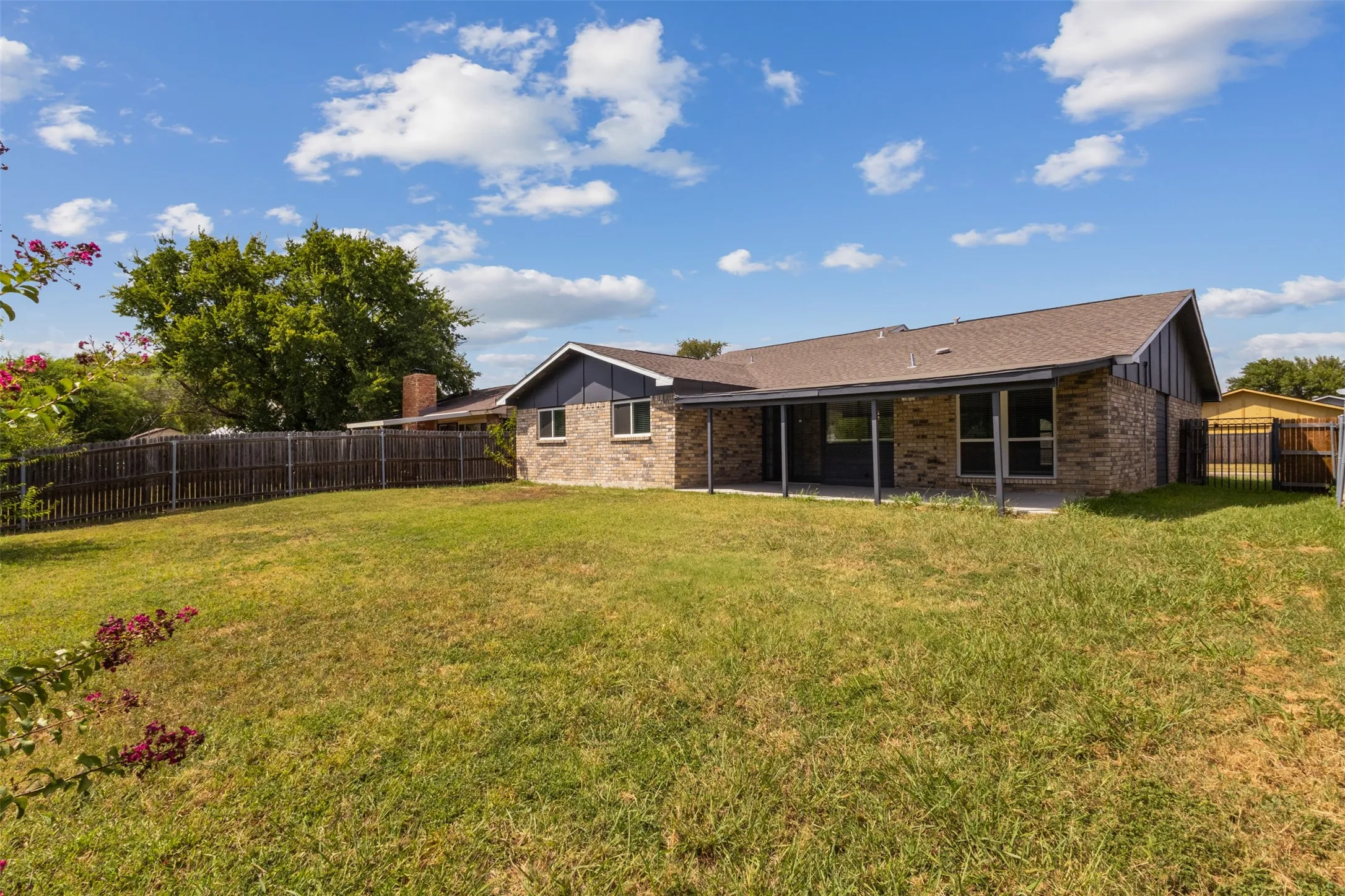 Expansive backyard with a wood privacy fence, brick exterior, covered patio, and mature trees