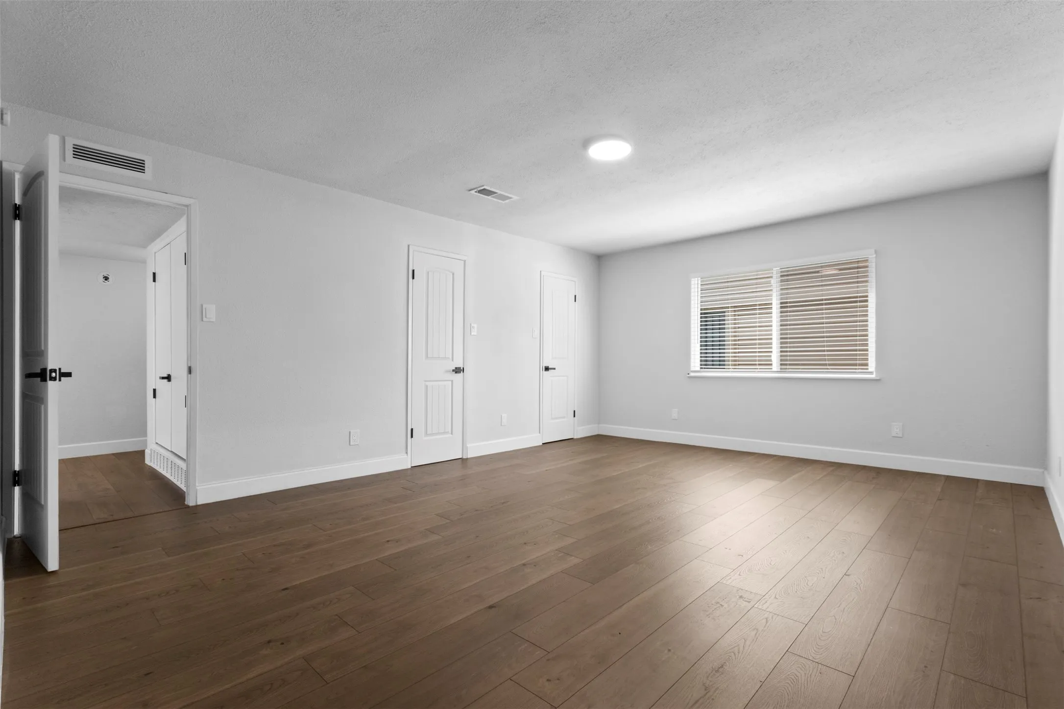 Expansive room featuring wood-finish flooring, white walls, and a large window with horizontal blinds