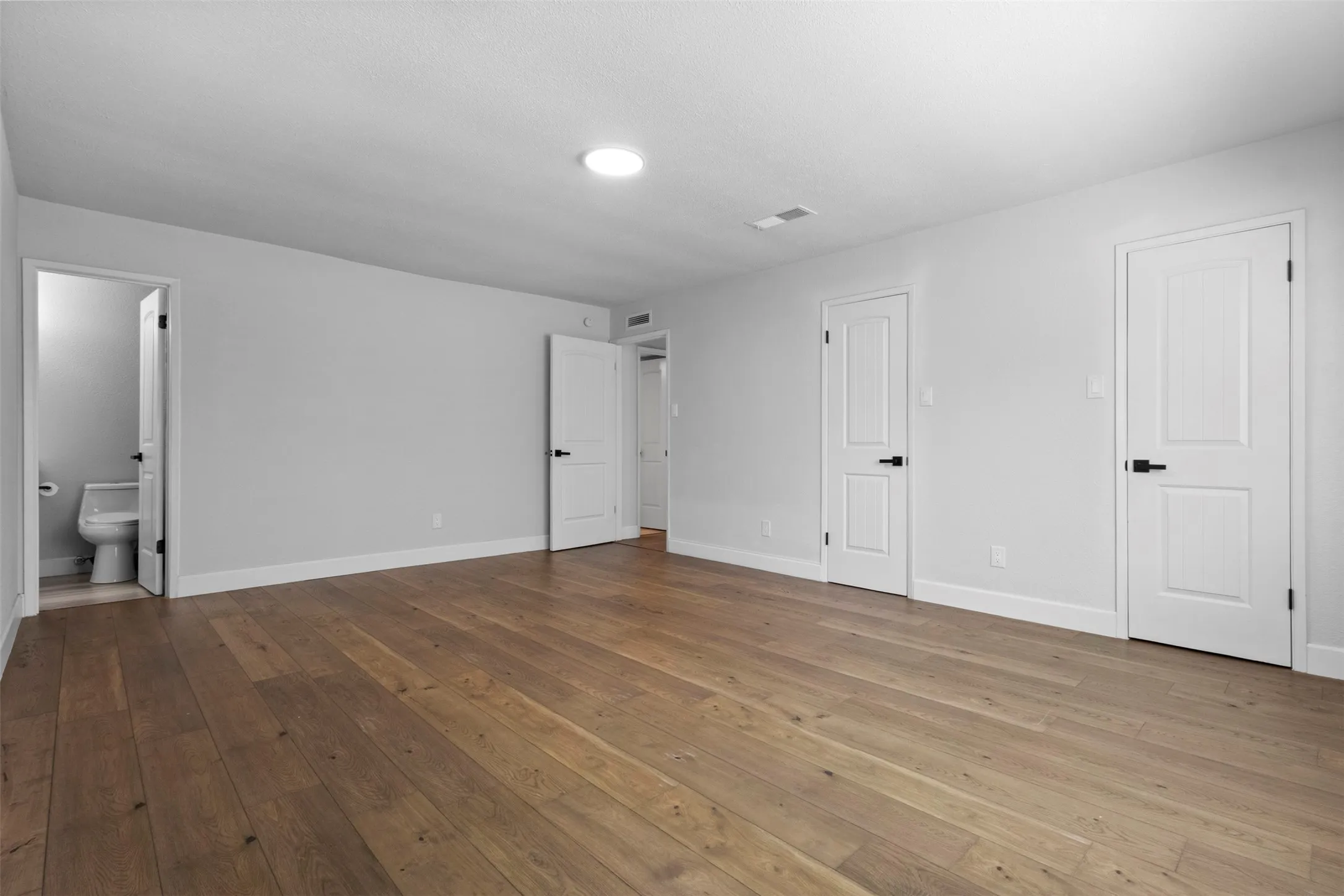 Spacious room featuring wood-finish flooring, light gray walls, white trim, and multiple panel doors with matte black hardware