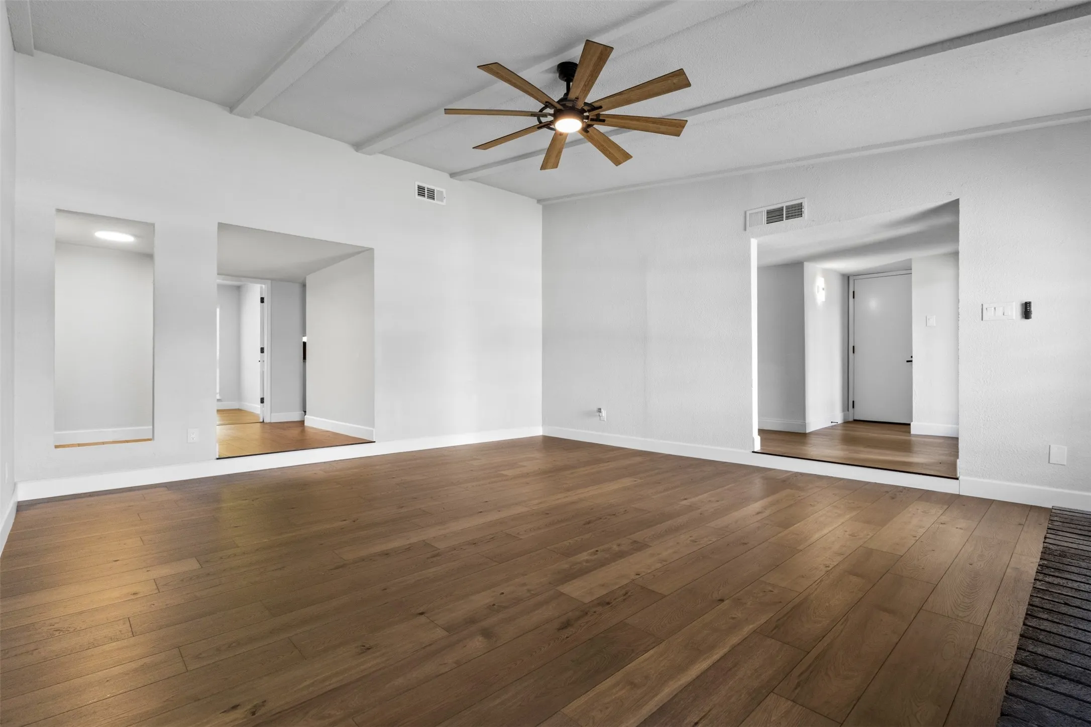 Wood-finish flooring throughout, bright white walls, recessed ceiling with exposed beams, and a ceiling fan with integrated lighting