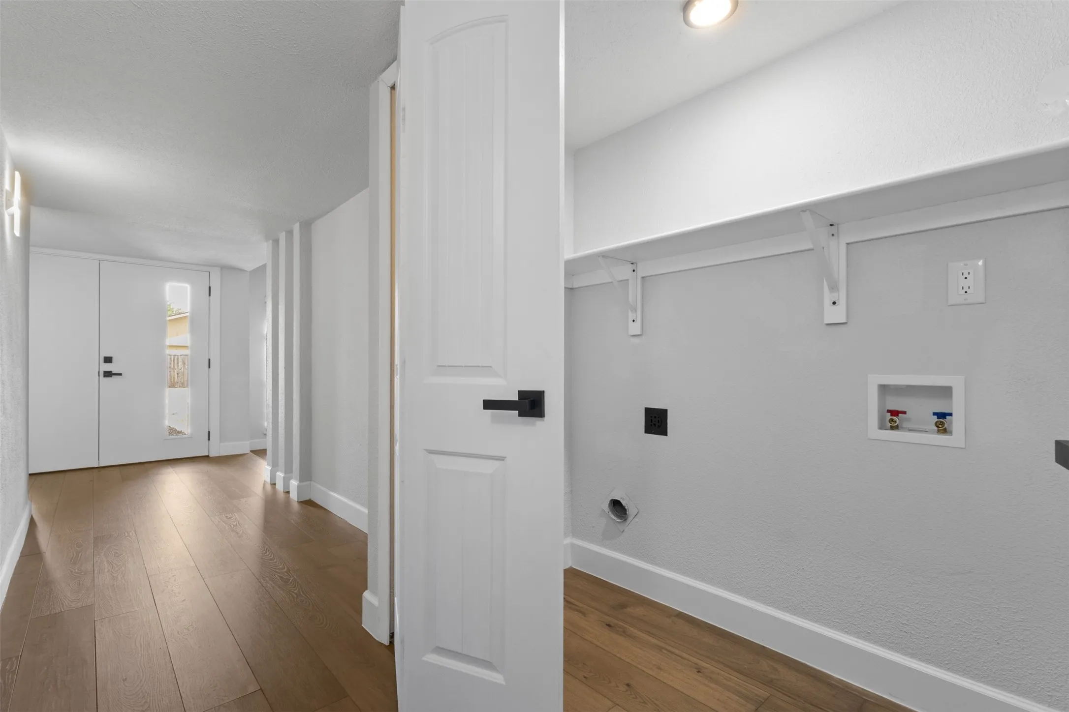 Wood-finish flooring throughout, white interior doors with matte black hardware, and an in-wall laundry hookup with storage shelving