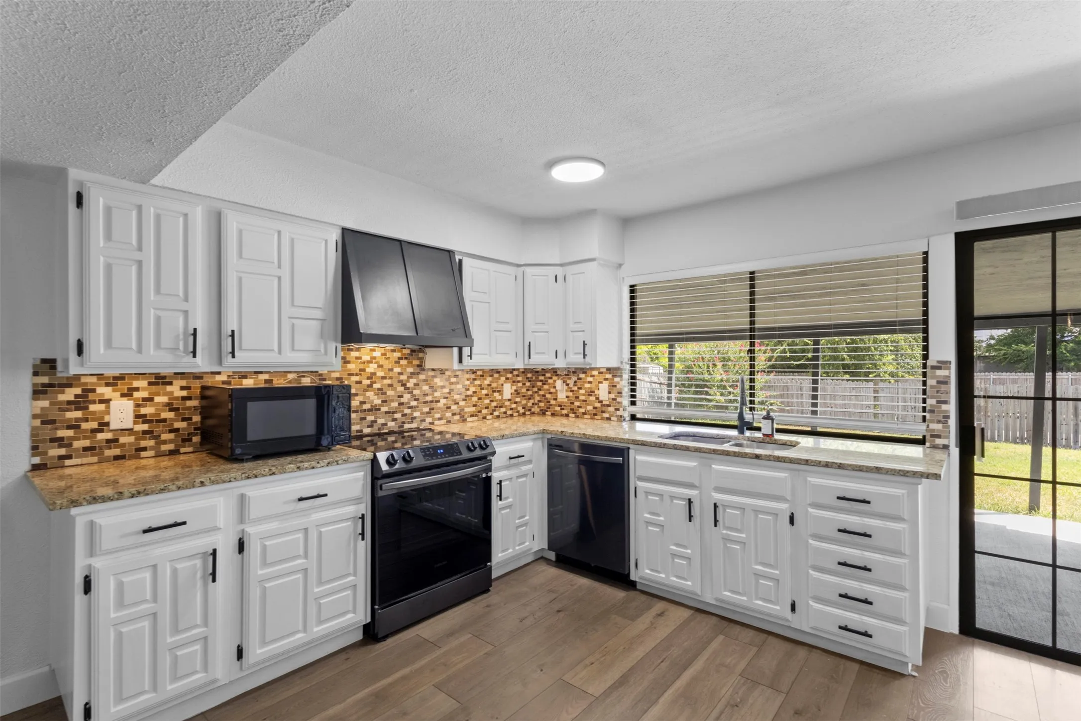 White cabinetry with dark hardware, stone countertops, mosaic tile backsplash, black appliances, and wood-finish flooring