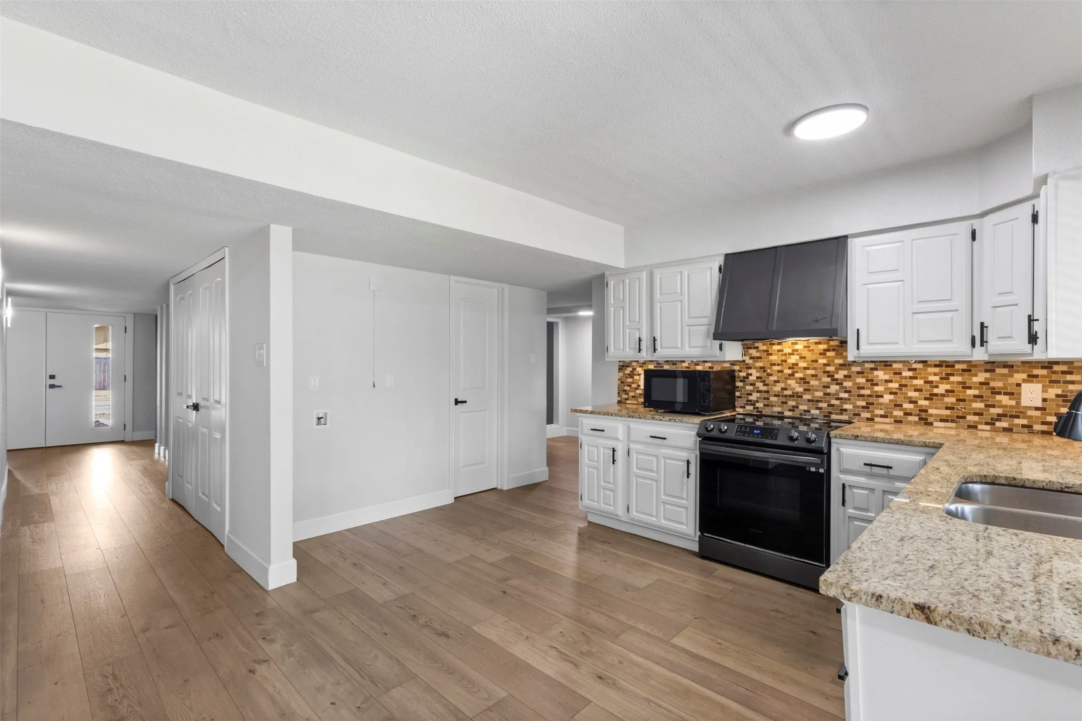 Kitchen featuring wood-finish flooring, white cabinetry, granite-style countertops, mosaic tile backsplash, and stainless steel appliances