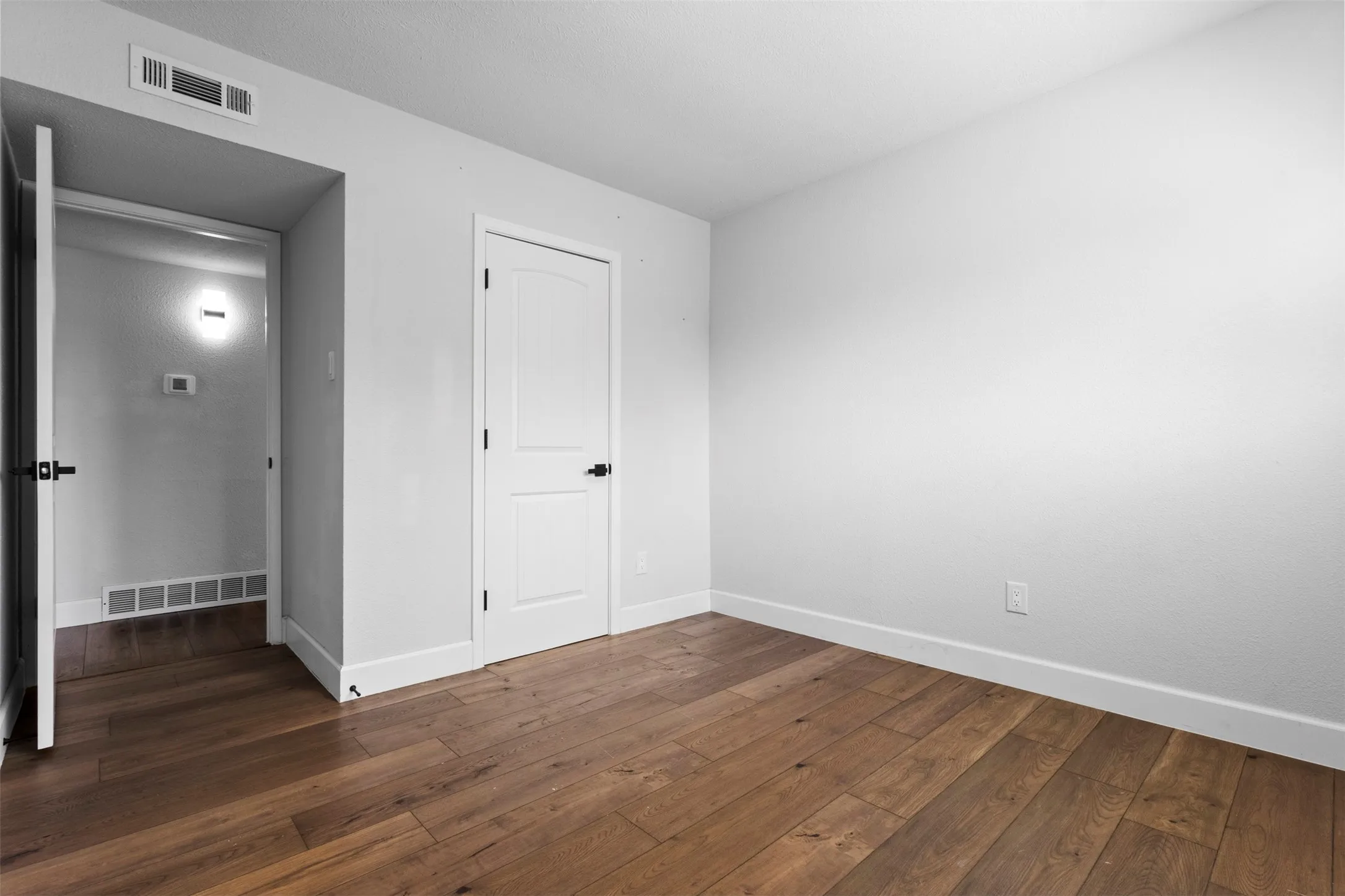 Wood-finish flooring with crisp white baseboards, white walls, and a white interior door with matte black hardware