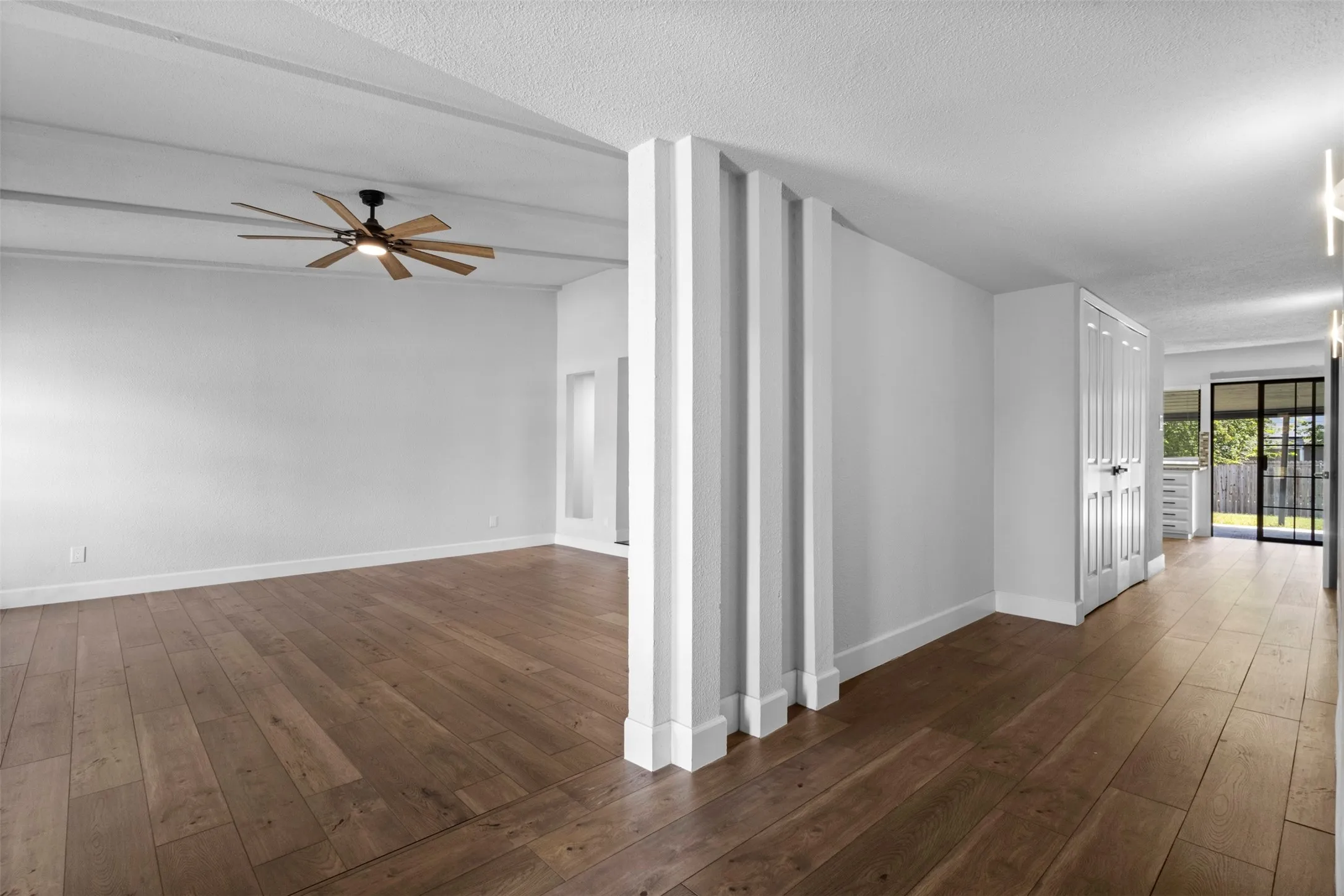 Expansive room featuring wood-finish flooring, a ceiling fan with integrated lighting, and a partial wall with decorative vertical panels