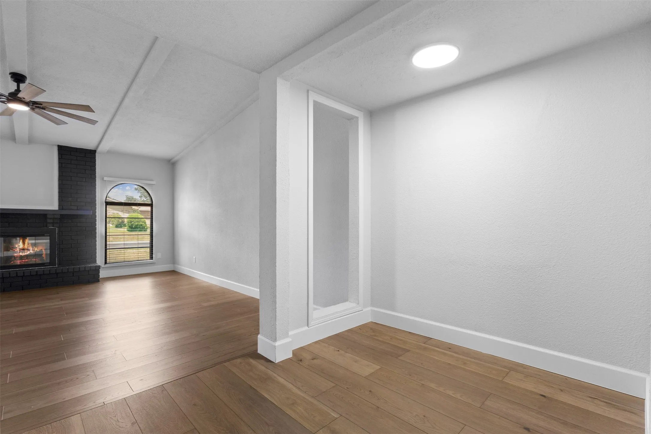 Wood-finish flooring, vaulted ceilings, black brick fireplace, arched window, and a ceiling fan