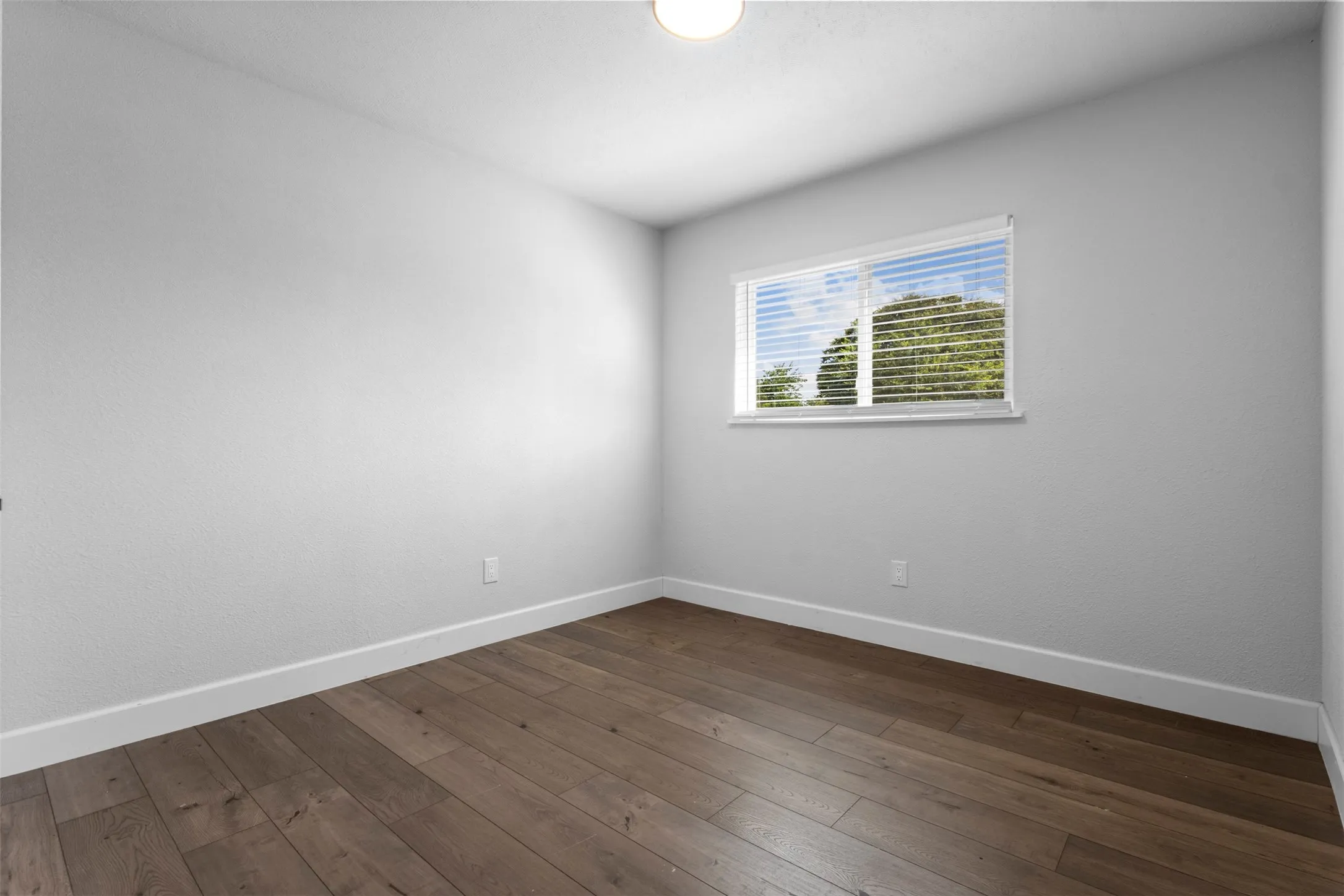 Wood-finish flooring, white painted walls, single window with blinds, and flush-mount ceiling light