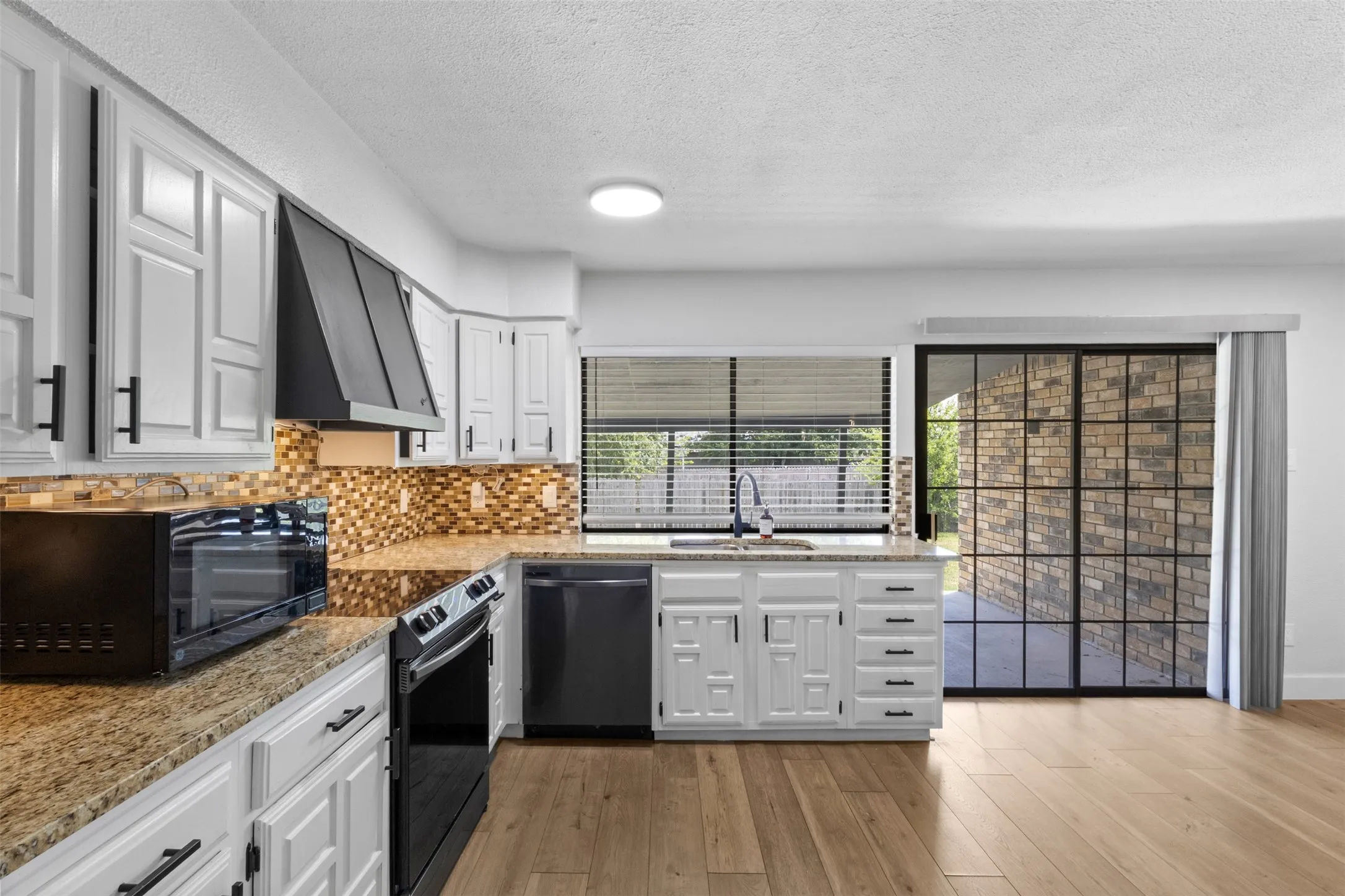 Kitchen featuring white cabinetry, granite-style countertops, a mosaic tile backsplash, black appliances, and wood-finish flooring