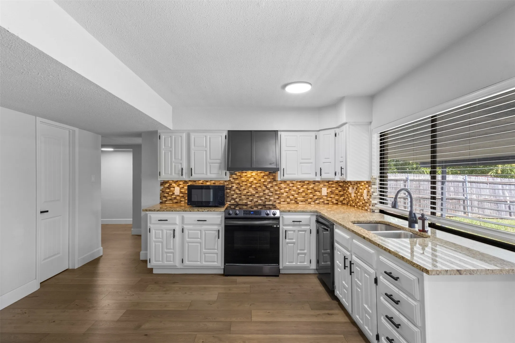Kitchen featuring light wood-finish flooring, white cabinetry with dark hardware, granite countertops, and a mosaic tile backsplash