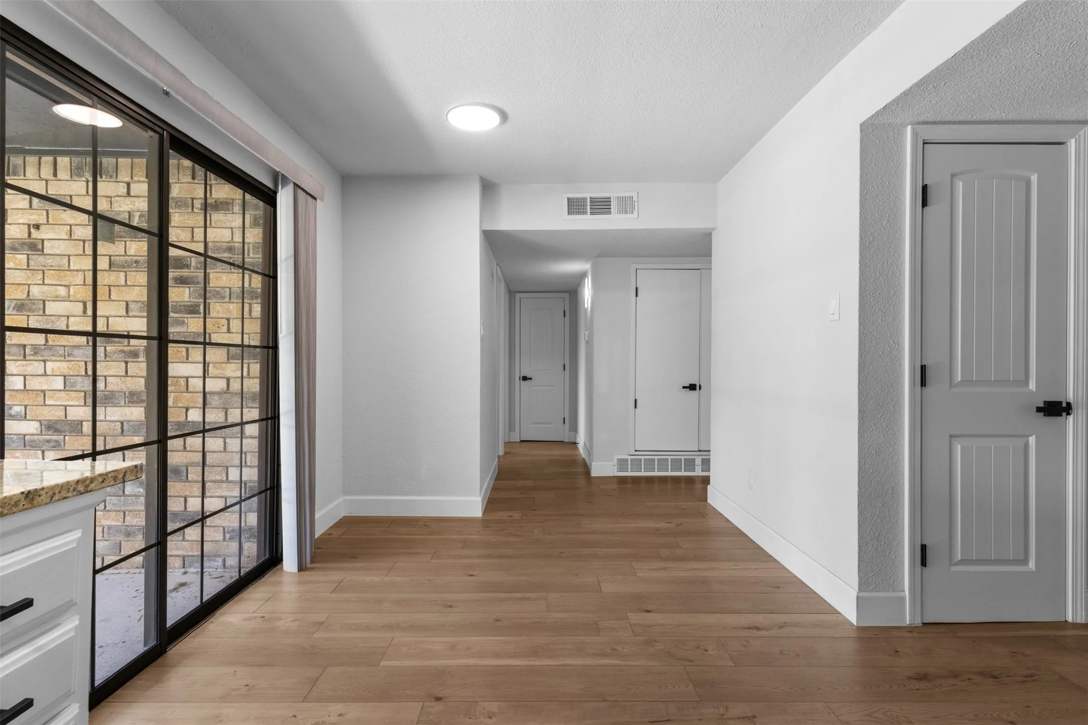 Spacious hallway showcasing warm wood-finish flooring throughout, abundant natural light from large multi-pane windows, and multiple six-panel doors providing access to adjoining spaces