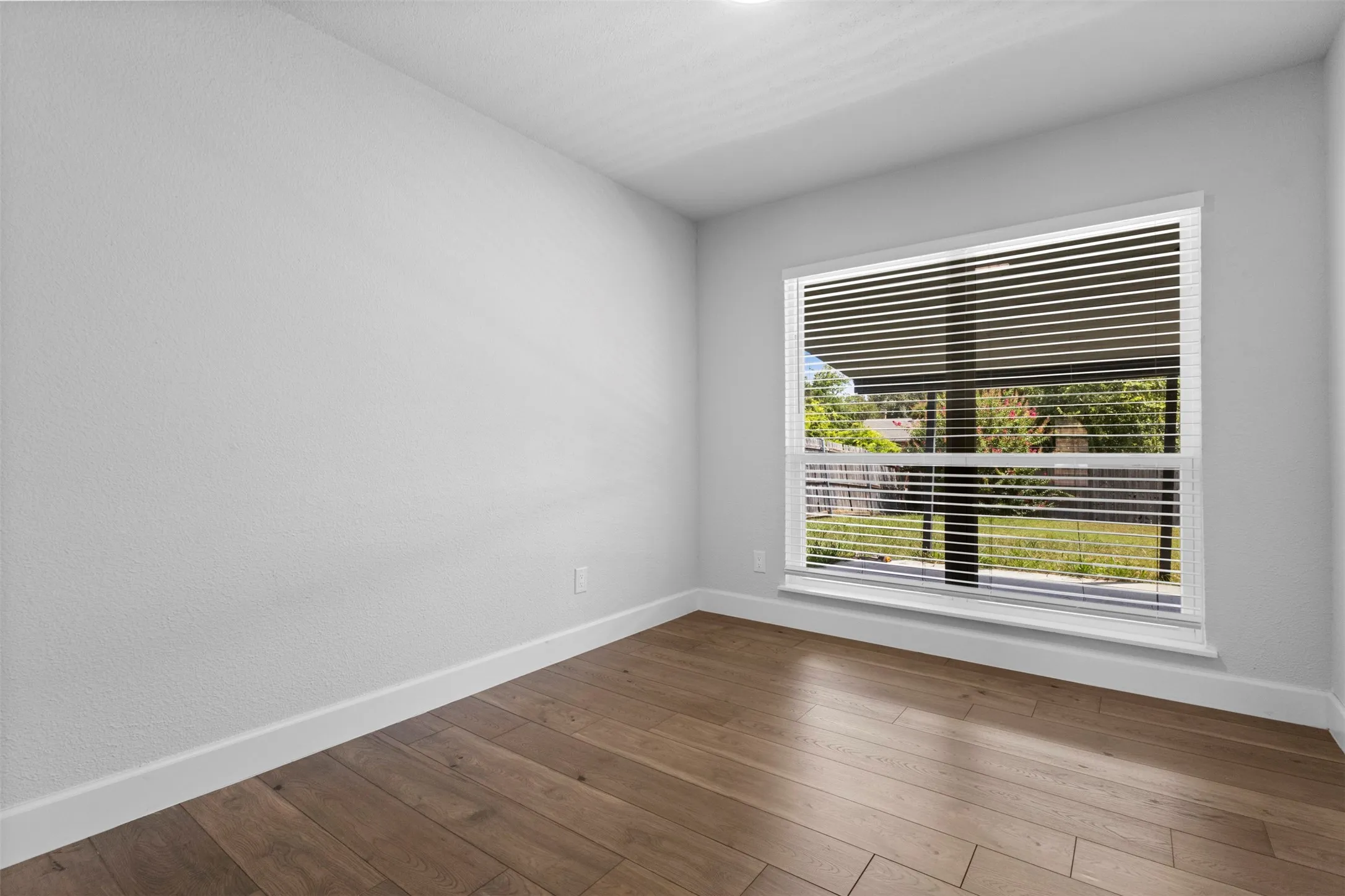 Wood-finish flooring with white trim and a window featuring horizontal blinds