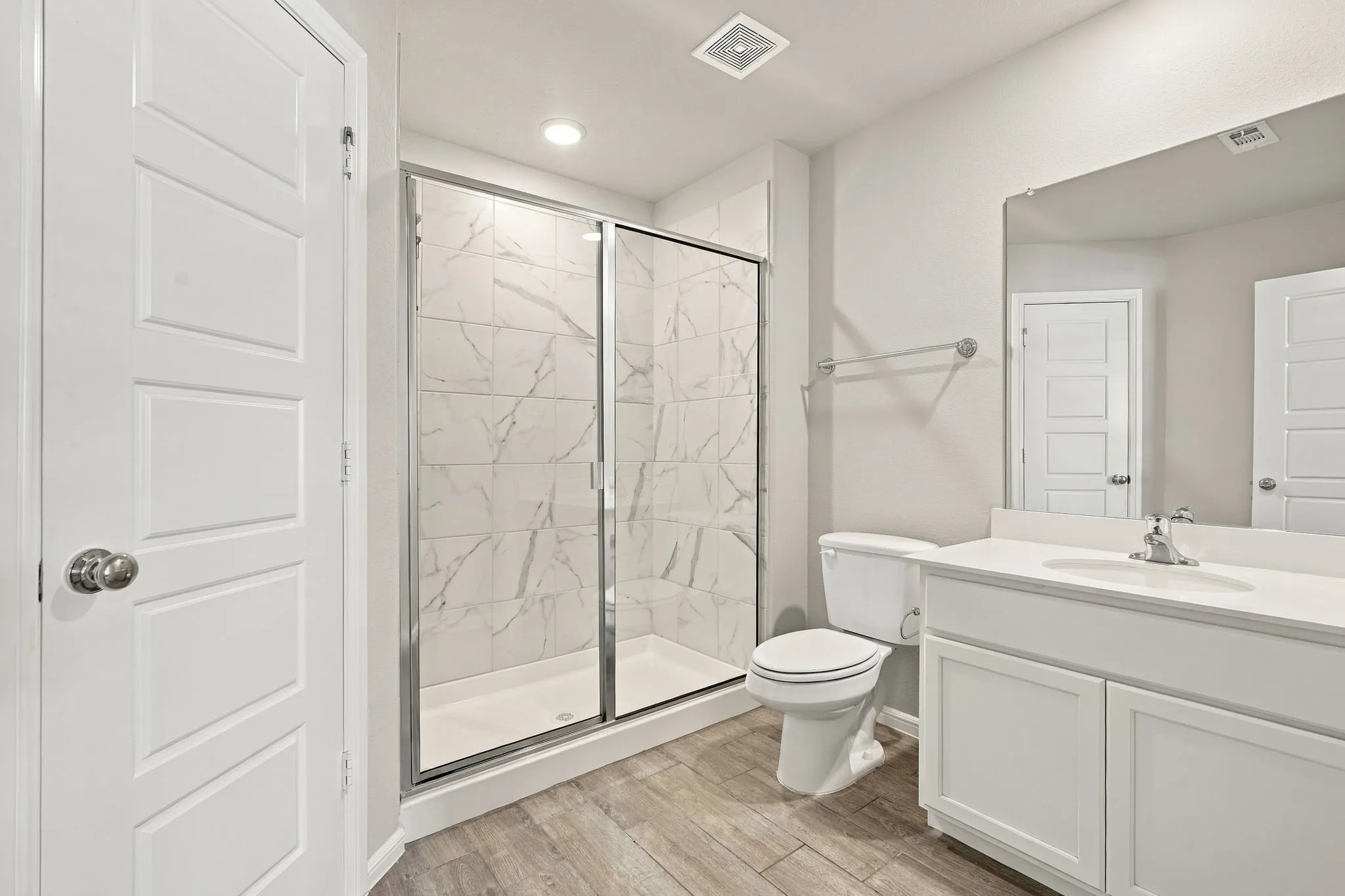 Shower with sliding glass enclosure, wood-finish flooring, single vanity with white countertop, and recessed lighting