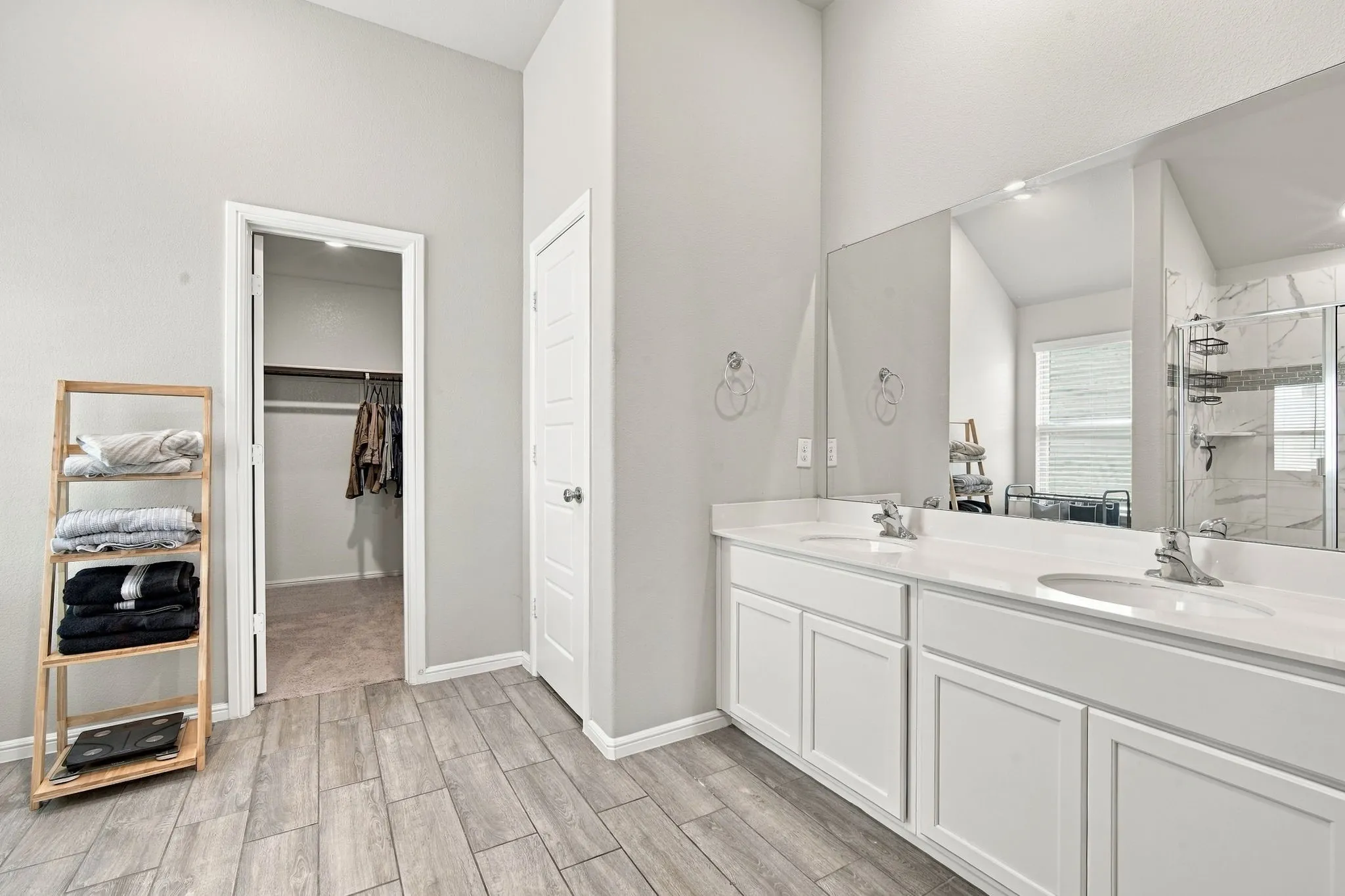 Dual vanity with white cabinetry, white countertops, wood-finish flooring, and a walk-in shower with glass enclosure
