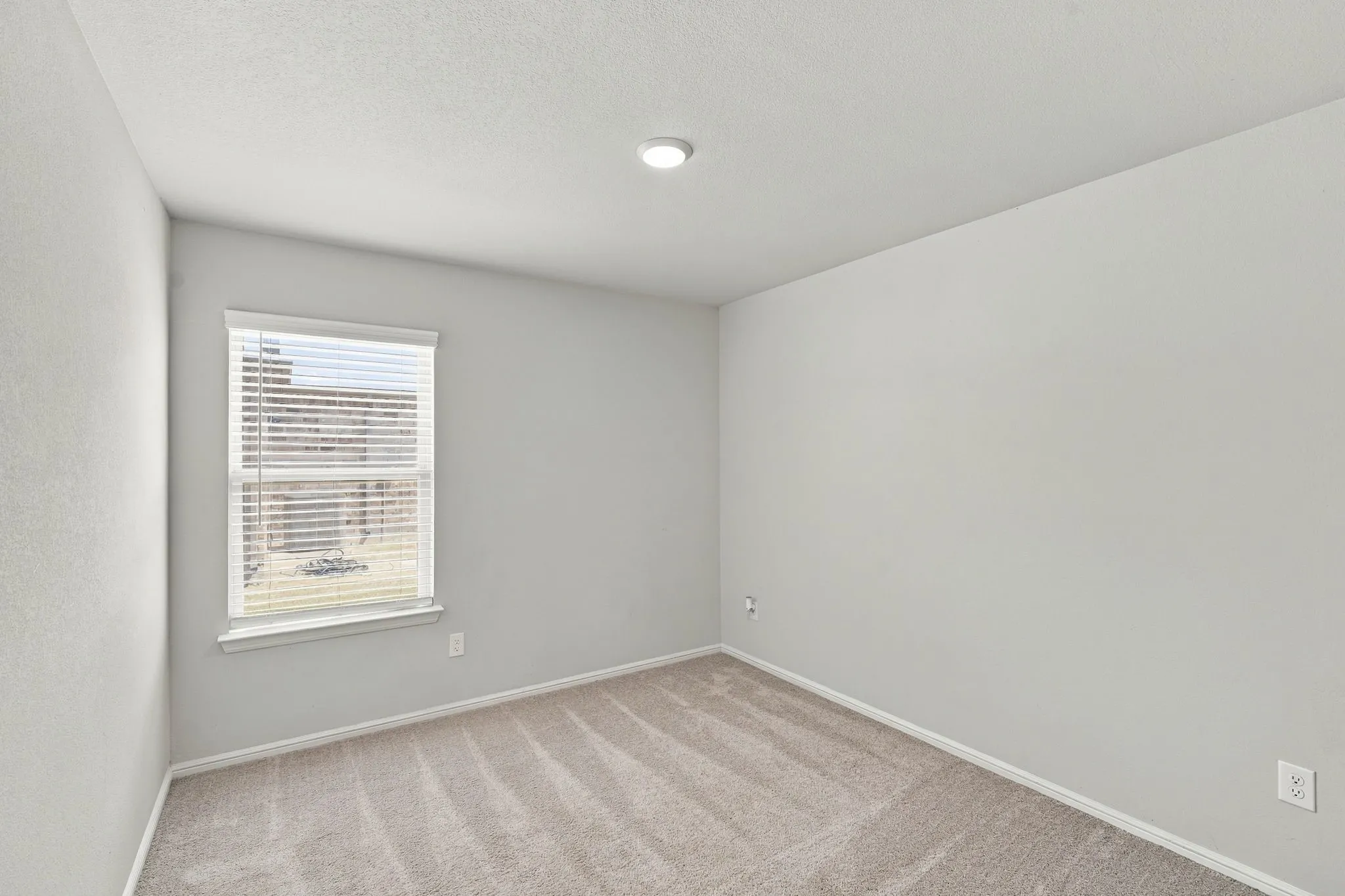 Recessed ceiling lighting, neutral carpet flooring, white walls, and a window with blinds