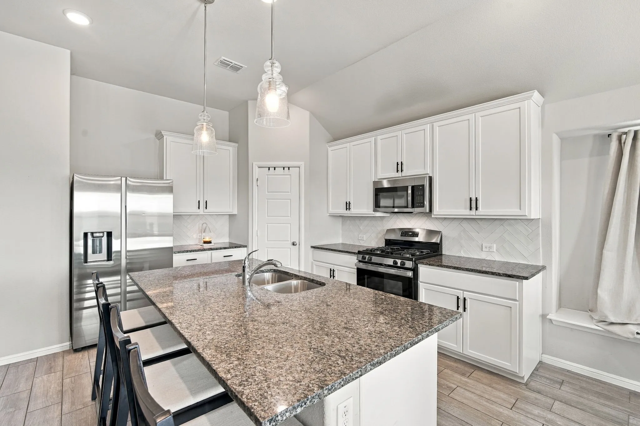 Kitchen featuring an oversized island with a double basin sink, granite countertops, stainless steel appliances, and white shaker-style cabinetry with matte black hardware
