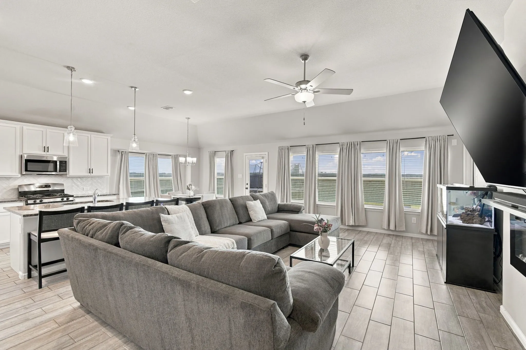 Open-concept living space featuring wood-finish flooring, recessed lighting, a ceiling fan, and multiple windows